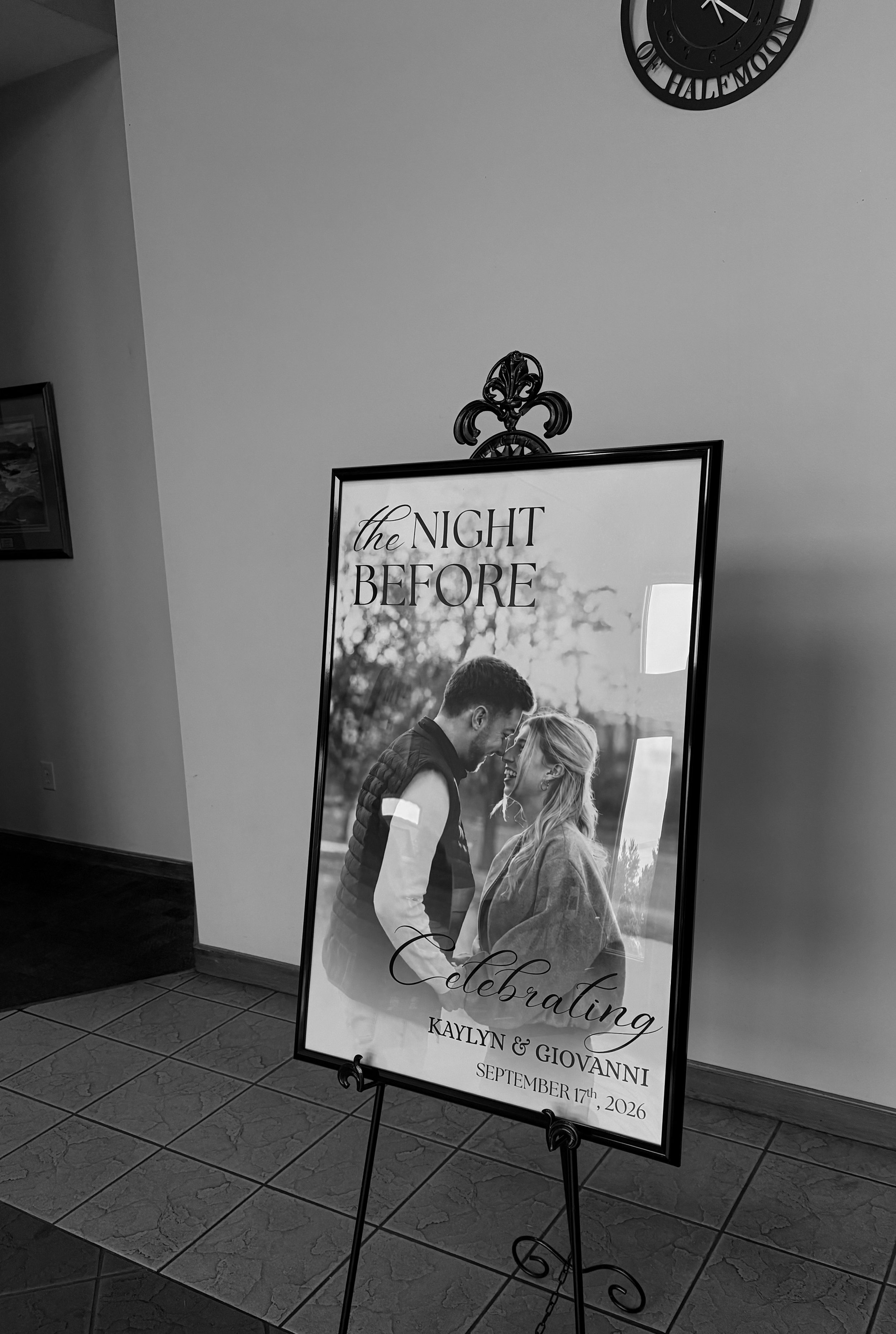 A large wedding celebration poster featuring a black and white photo of a couple embracing, with the text "the NIGHT BEFORE" at the top, and details below: "Celebrating KAYLYN & GIOVANNI, September 17th, 2026." The poster is displayed on a decorative