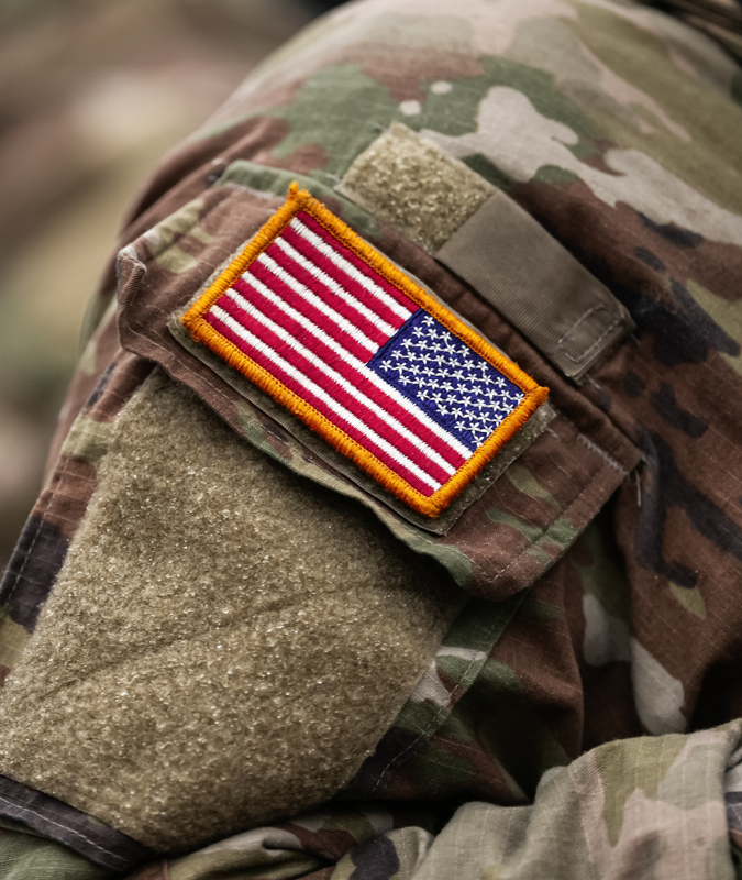 Close-up of a soldier's camouflage uniform with an American flag patch on the sleeve.