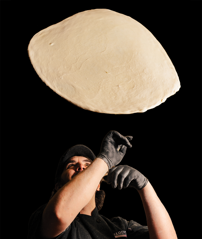 A person tossing a large piece of dough into the air