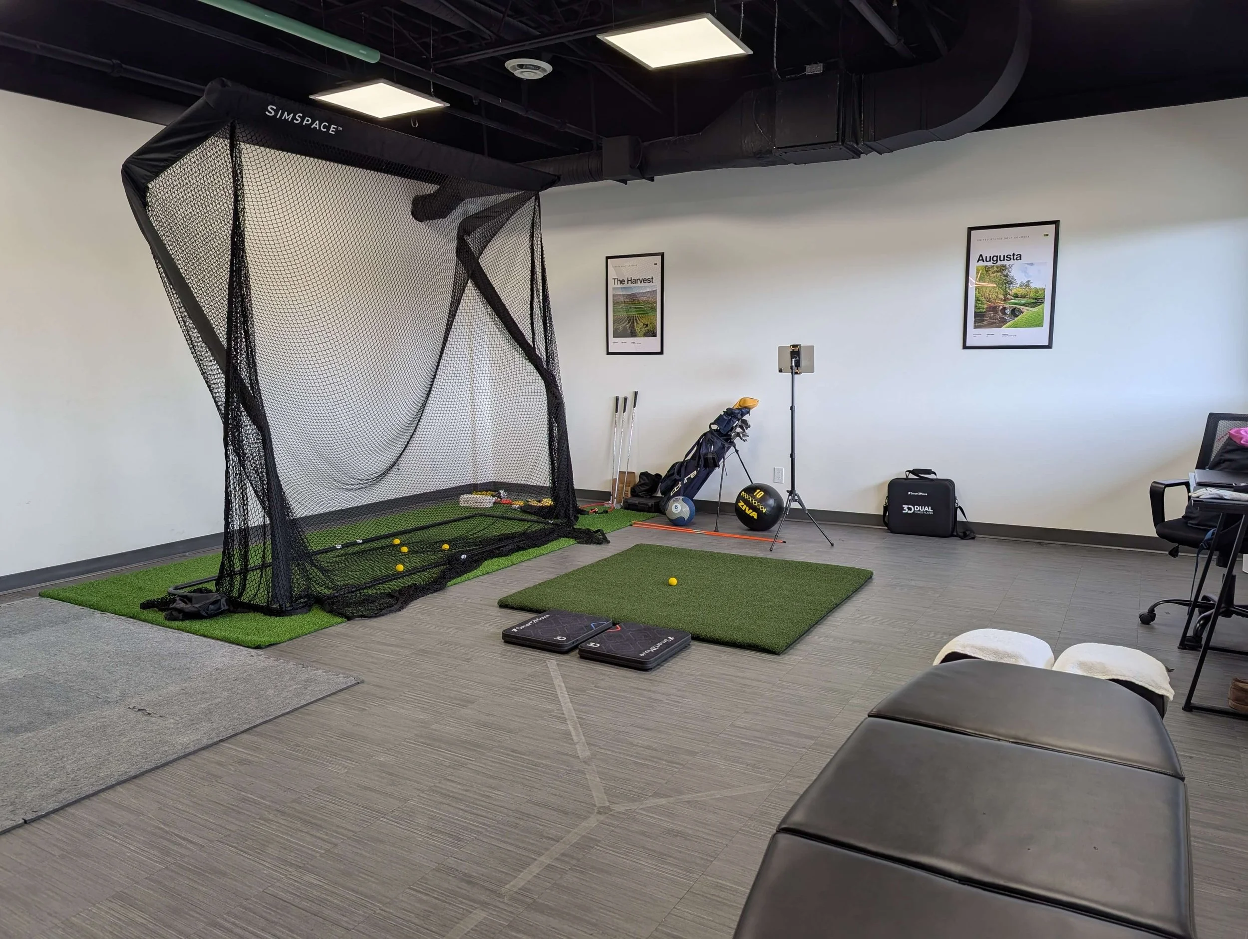 Indoor golf practice area with a large black net, golf balls, golf clubs, golf mat, and training equipment including a golf simulator setup.