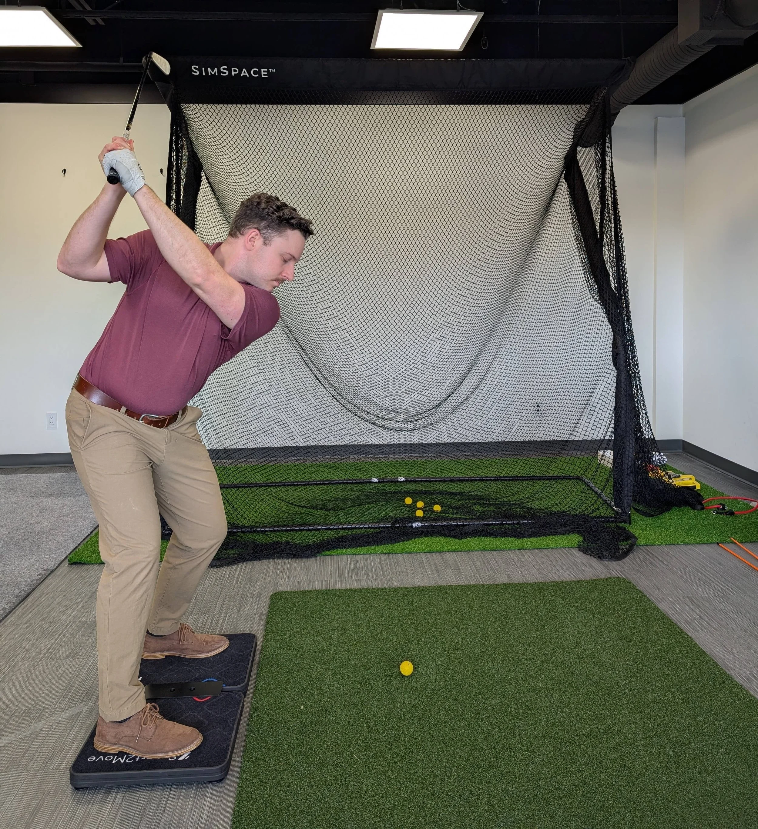 Man getting a golf lesson indoors using a simulator with a net and golf balls.