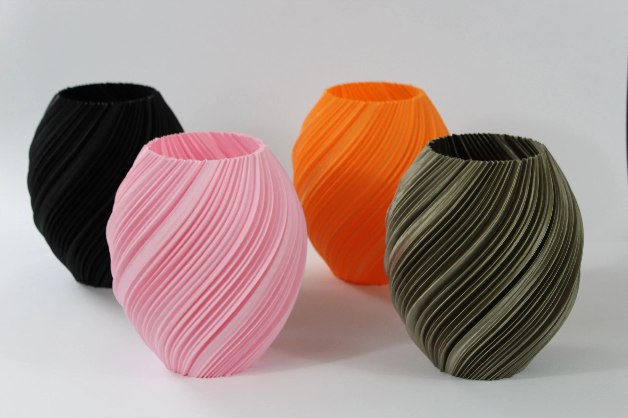 Cinque vasi di terracotta con superficie texture a righe incise, di colore nero, rosa, arancione e verde oliva, disposti su sfondo bianco.