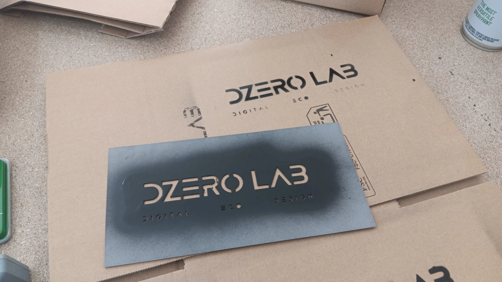 Cartello con il logo 'ZERO LAB DIGITAL S.O. DESIGN' su una superficie di cartone, probabilmente sito di produzione o di design.