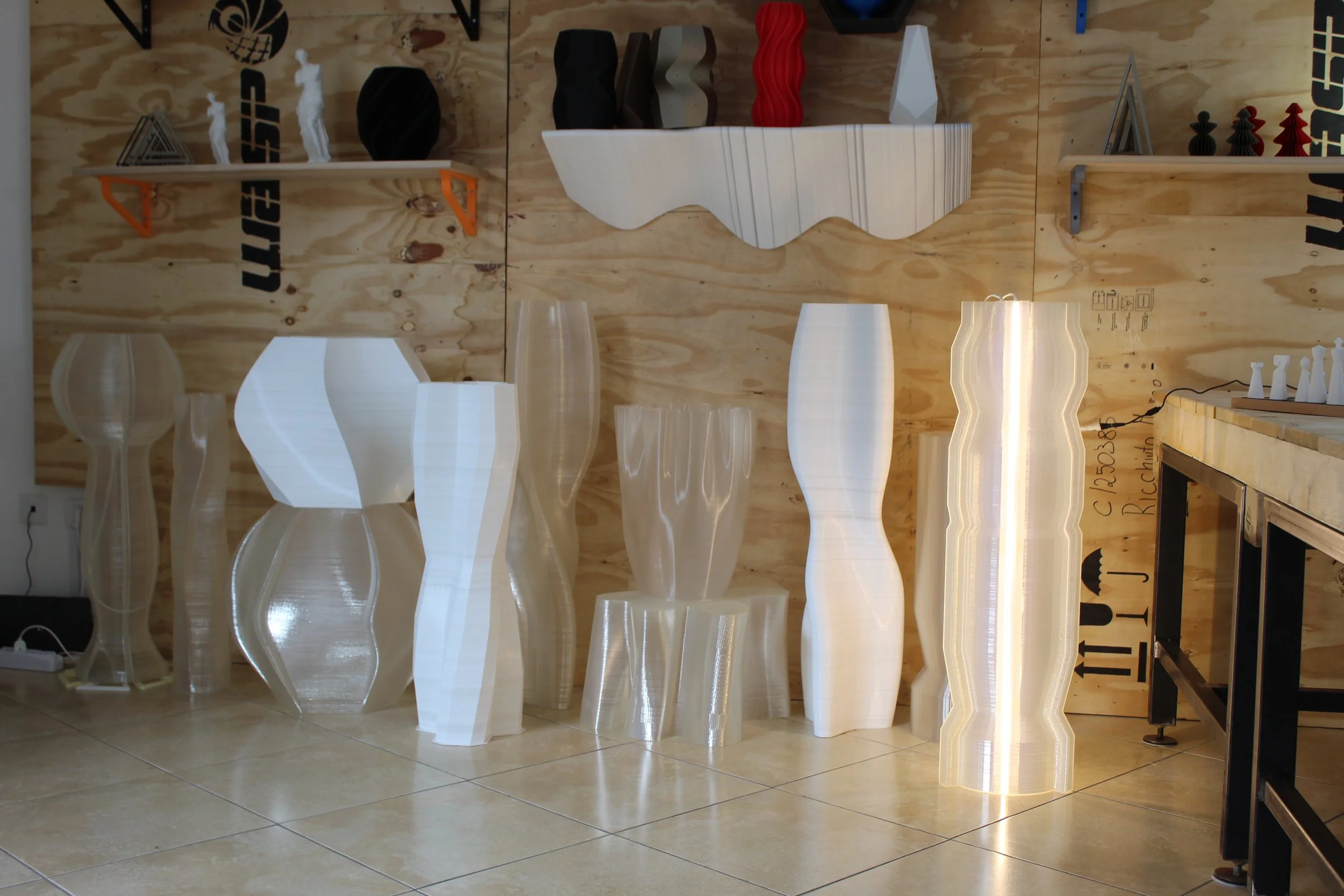 Vasi e lampade di design bianco e trasparente su pavimento in piastrelle con parete in legno sullo sfondo.