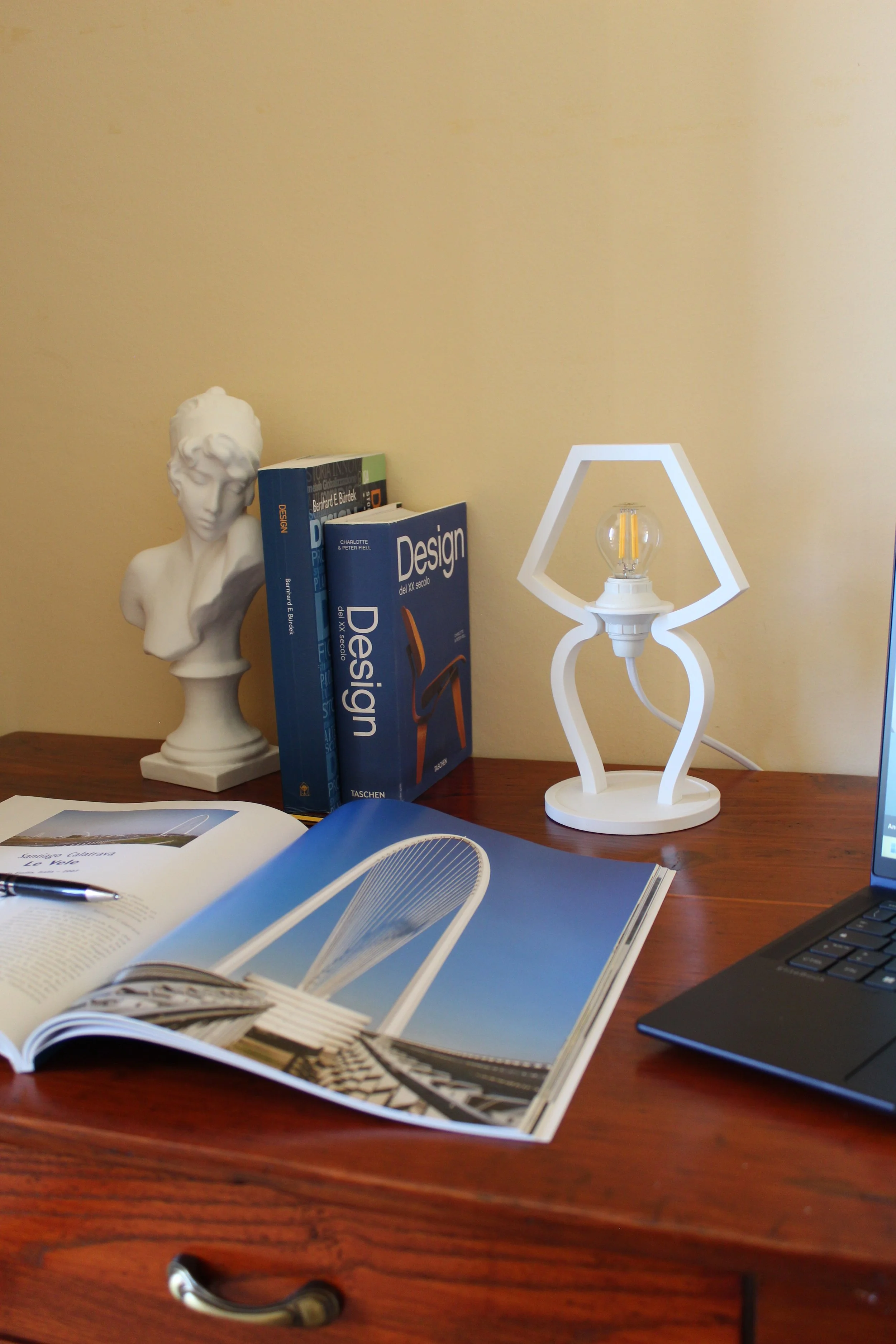 Scrivania con libri di design, statua, lampada e computer portatile.