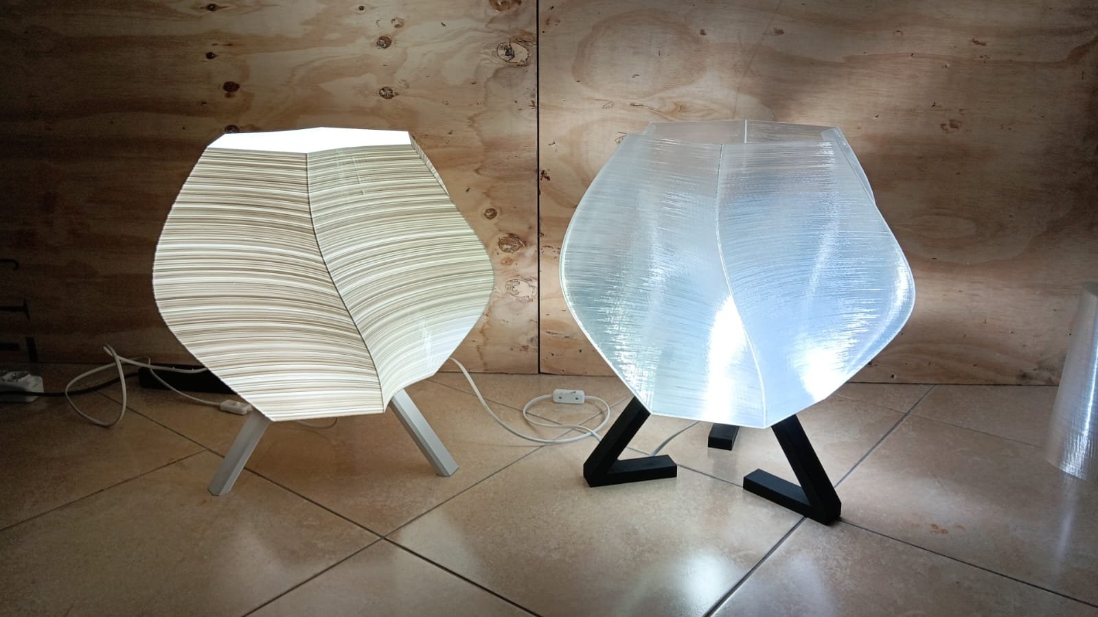 Lampade da tavolo moderne con base di legno e paralumi trasparenti, una con paralume bianco con linee sottili e l'altra con paralume trasparente con texture a strisce.