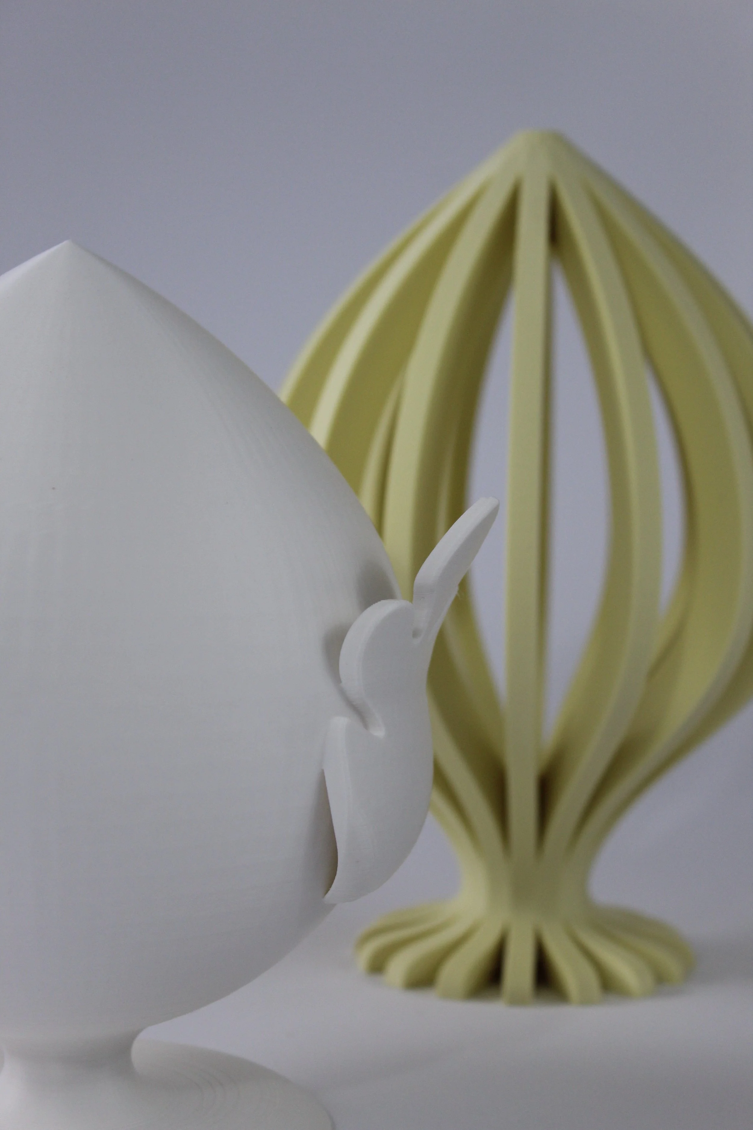 Modellini di una lampada e un oggetto decorativo con forma di uccello, realizzati in materiali leggeri in bianco e beige.