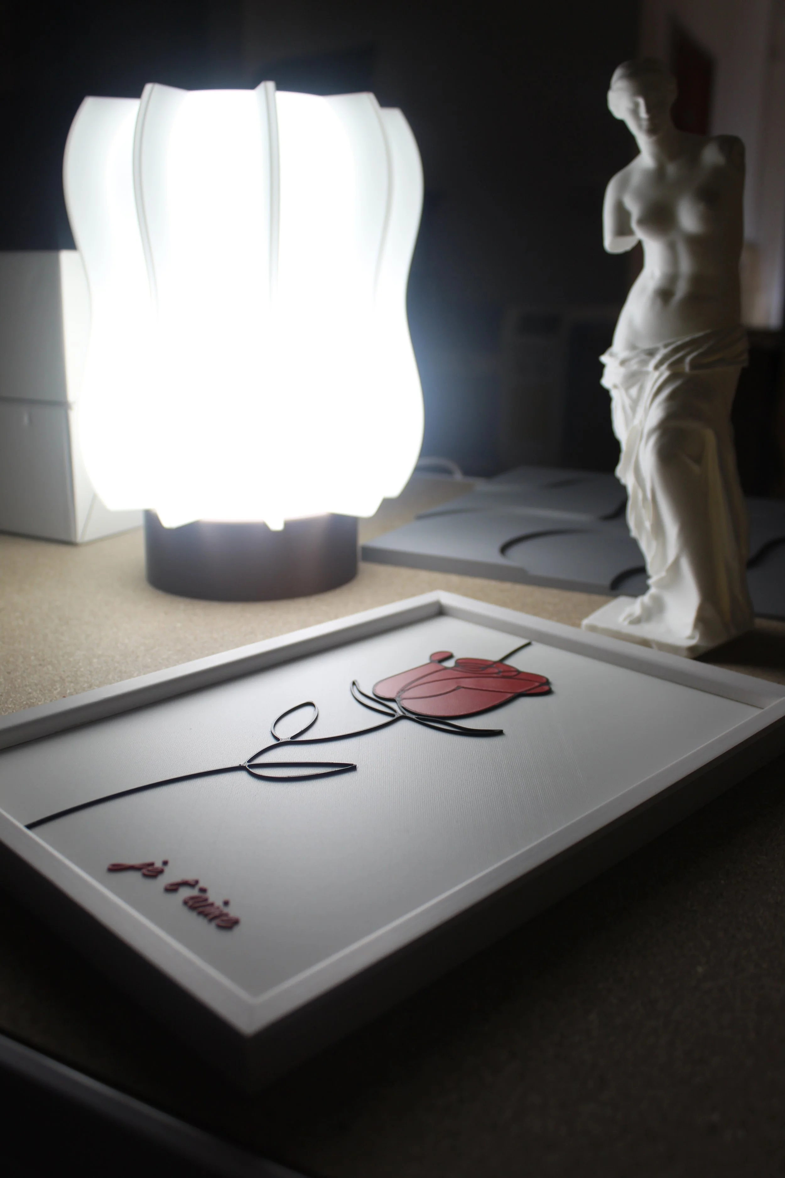 Una lampada accesa, una statua di marmo di una donna, un quadro con una rosa stilizzata e la scritta  fiori" in italiano.