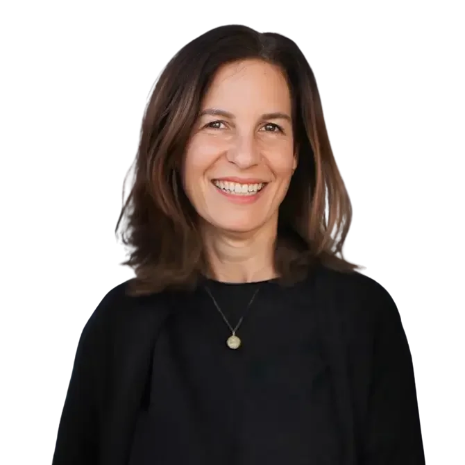 A woman with shoulder-length brown hair smiling and wearing a black top with a necklace, posing against a dark background.