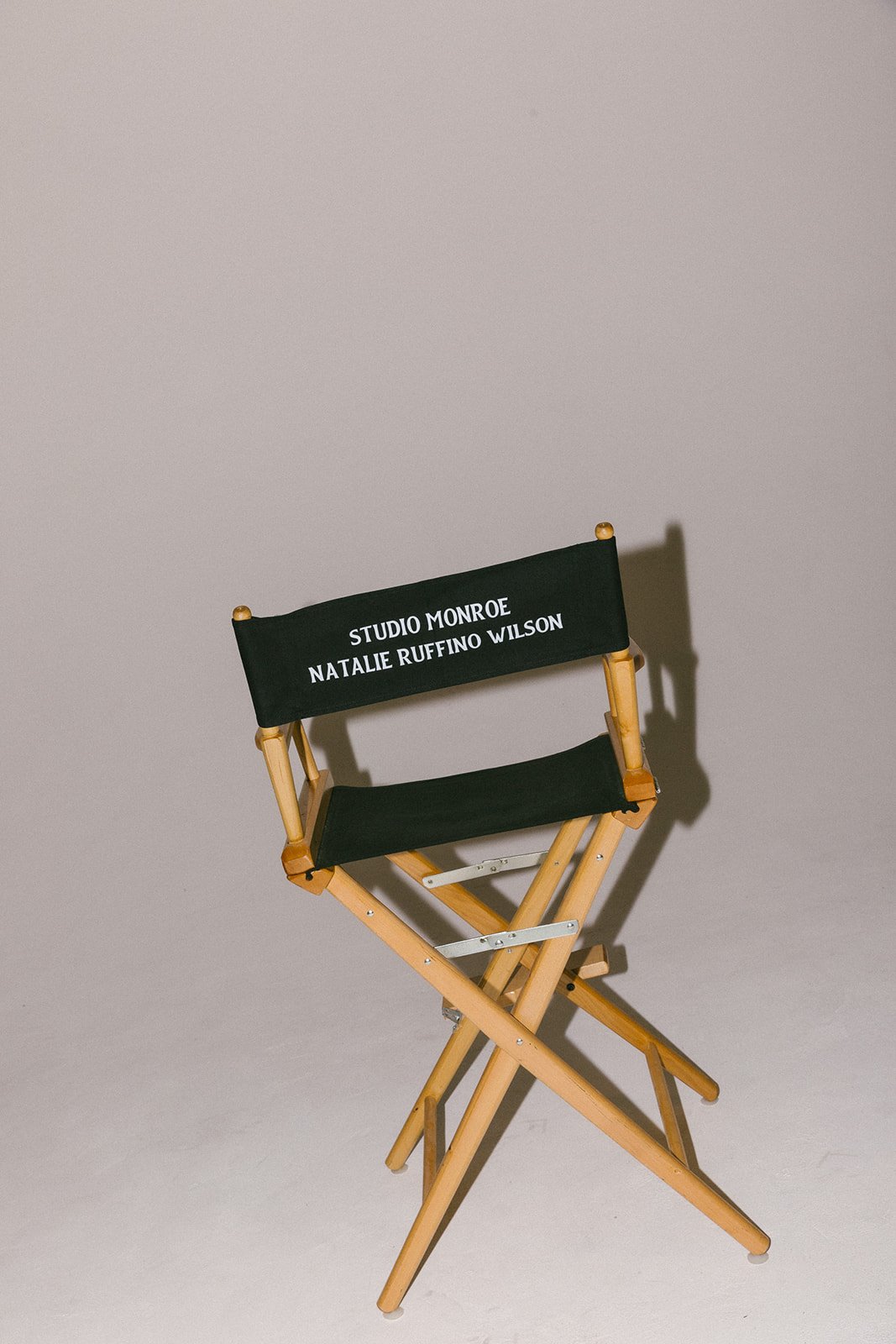 A black director's chair with wooden armrests and frame, with white text on the backrest reading 'Studio Monroe, Natalie Ruffino Wilson', set against a plain, light background.