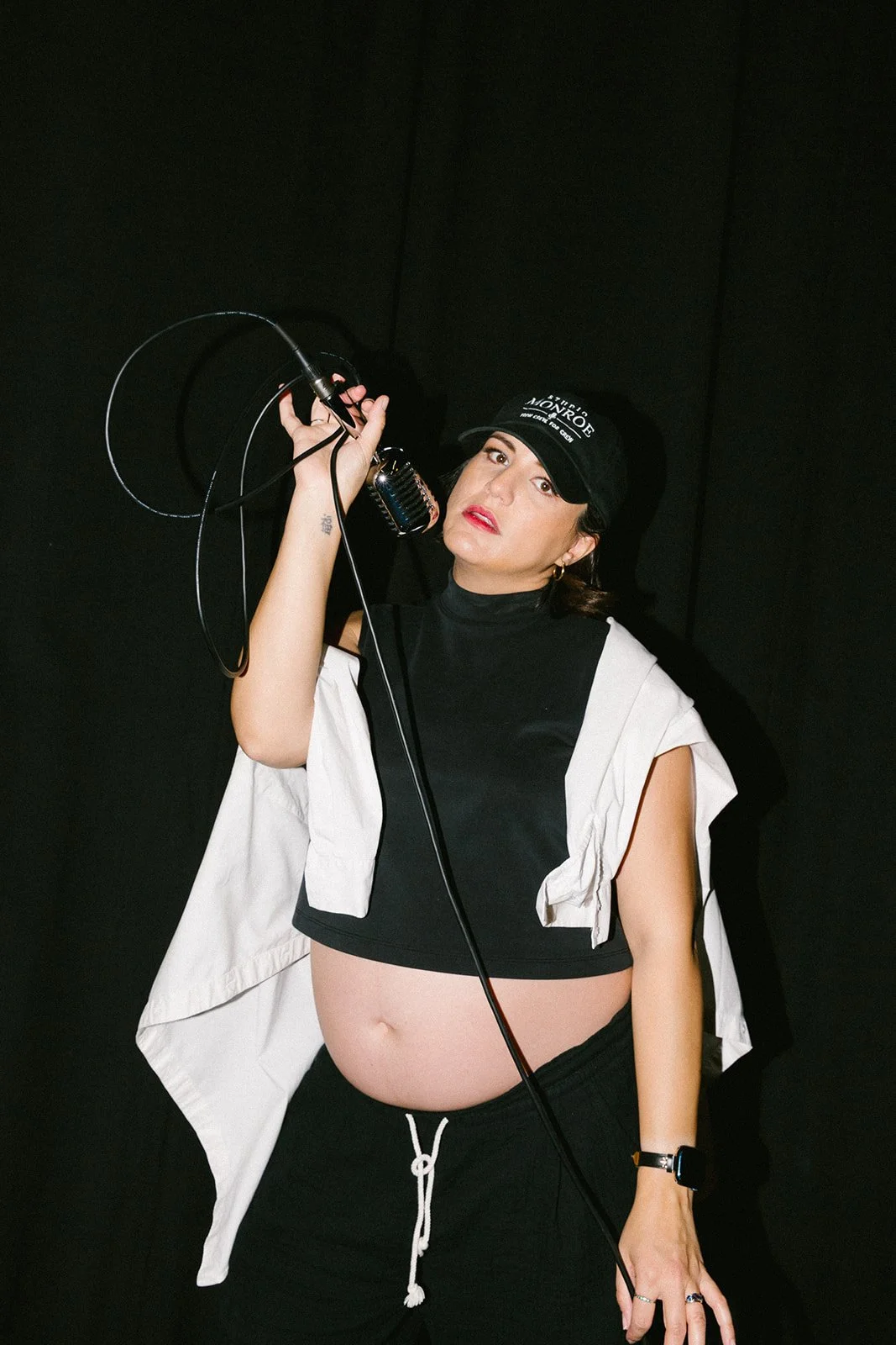 A woman in black and white clothing holding a microphone against a black background.