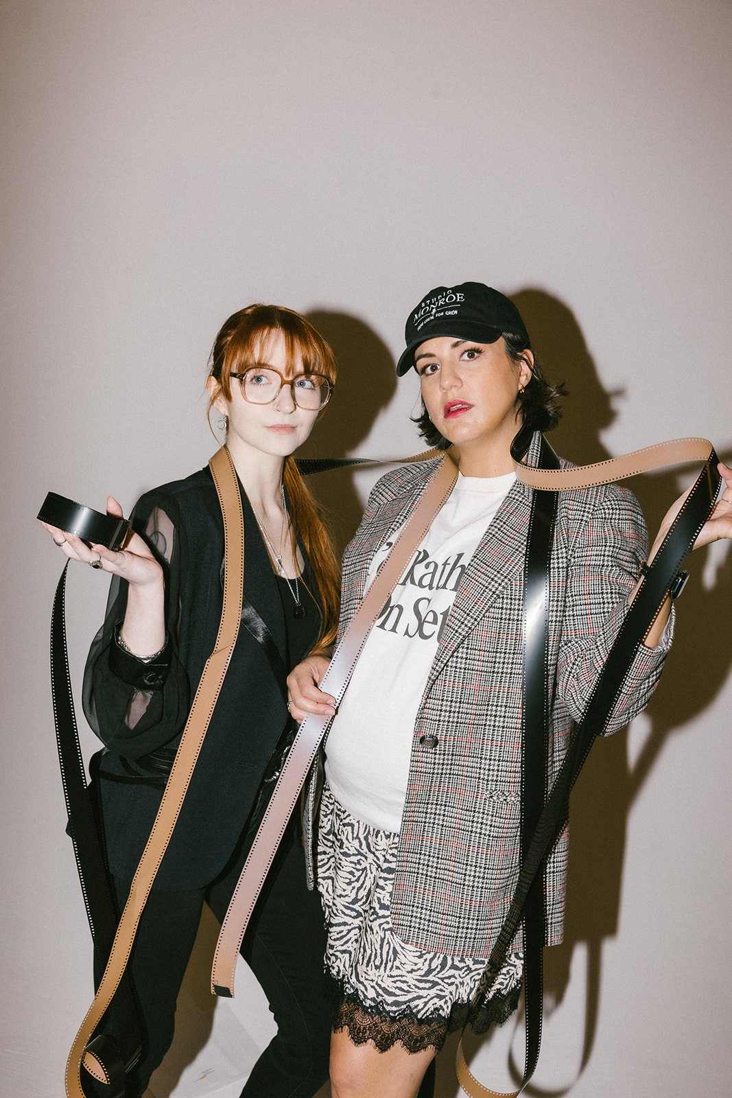 Two women standing together holding film strips and tape against a plain background.