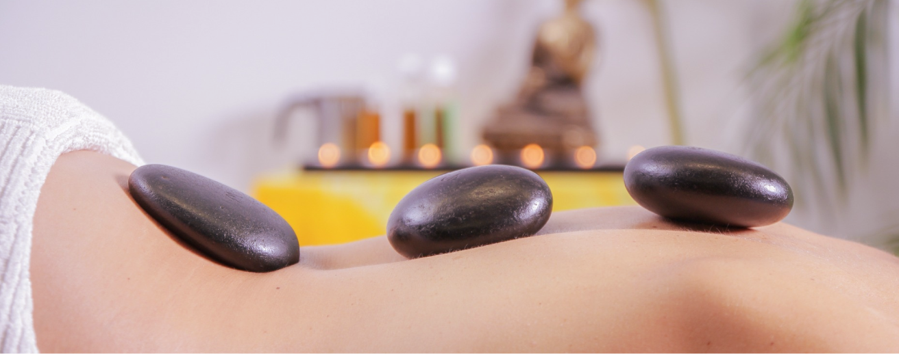 Hot stone massage therapy with smooth heated stones placed along the back, promoting deep relaxation, muscle relief, and a balanced, restorative experience.