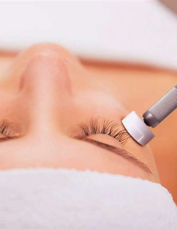 A person receiving an eyelash extension treatment with a tool applying adhesive to their natural eyelashes.