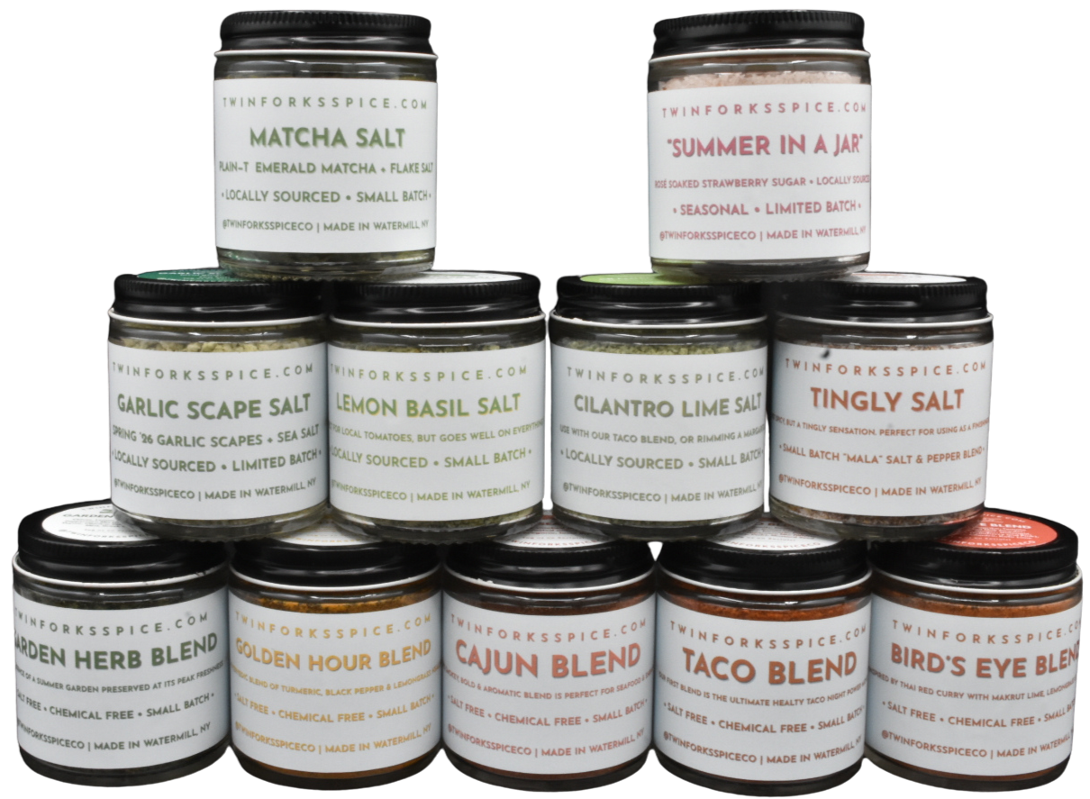 Stack of Twin Forks Spice seasoning jars, including matcha salt, summer-in-a-jar strawberry sugar, garlic scape salt, lemon basil salt, cilantro lime salt, tingly salt, garden herb blend, golden hour blend, Cajun blend, taco blend, and bird’s eye blend.