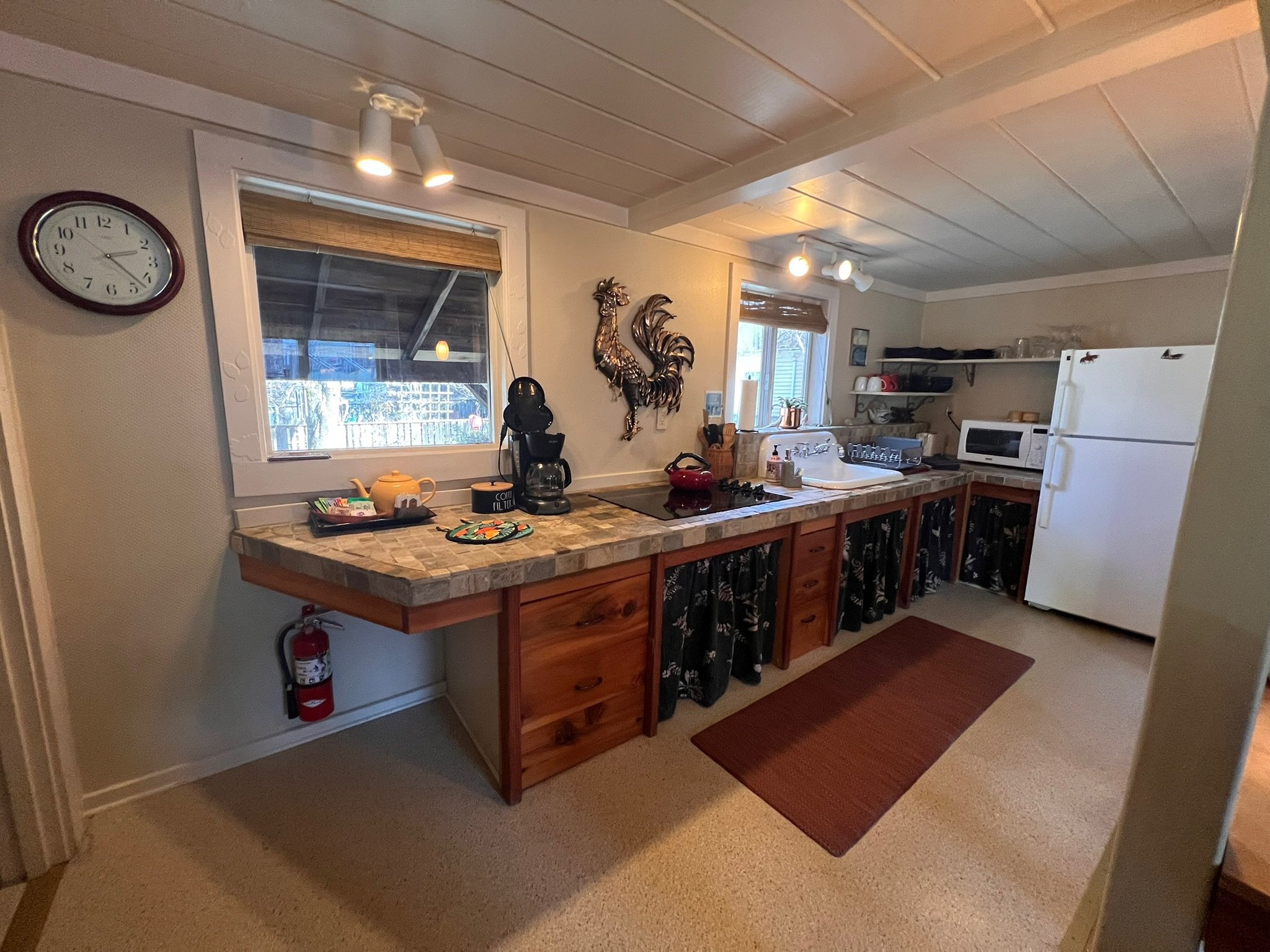 Cozy kitchen with wood accents, a white refrigerator, microwave, coffee maker, and decorative rooster wall art.