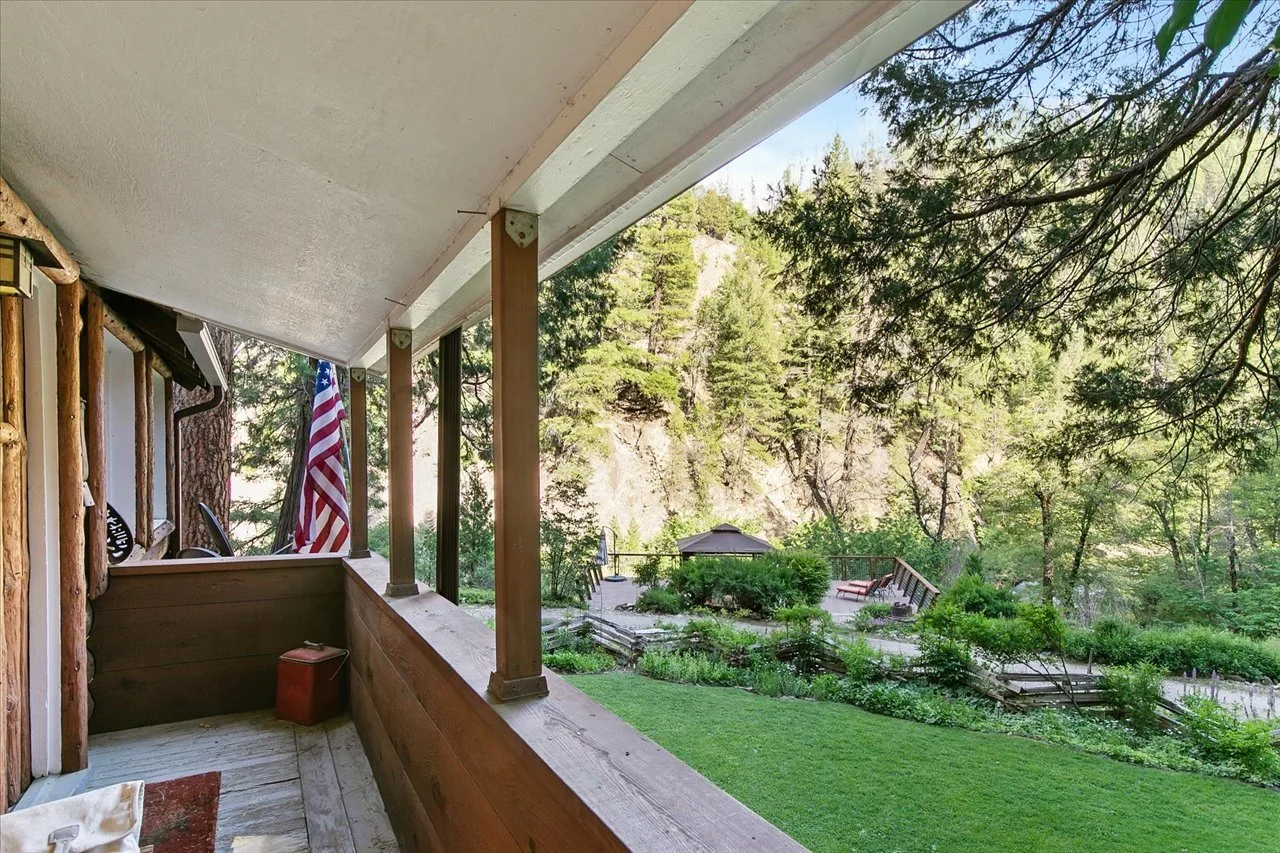 View from a wooden porch overlooking a lush green yard with trees and a small gazebo in the distance, surrounded by a forest landscape.