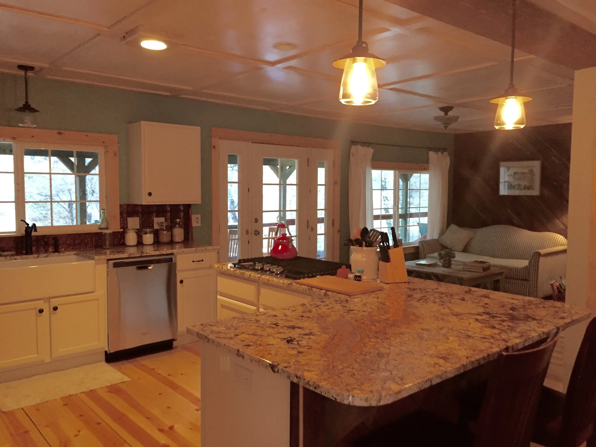 Cozy kitchen and living room with granite countertop island, wooden flooring, and a sitting area with sofa and coffee table.