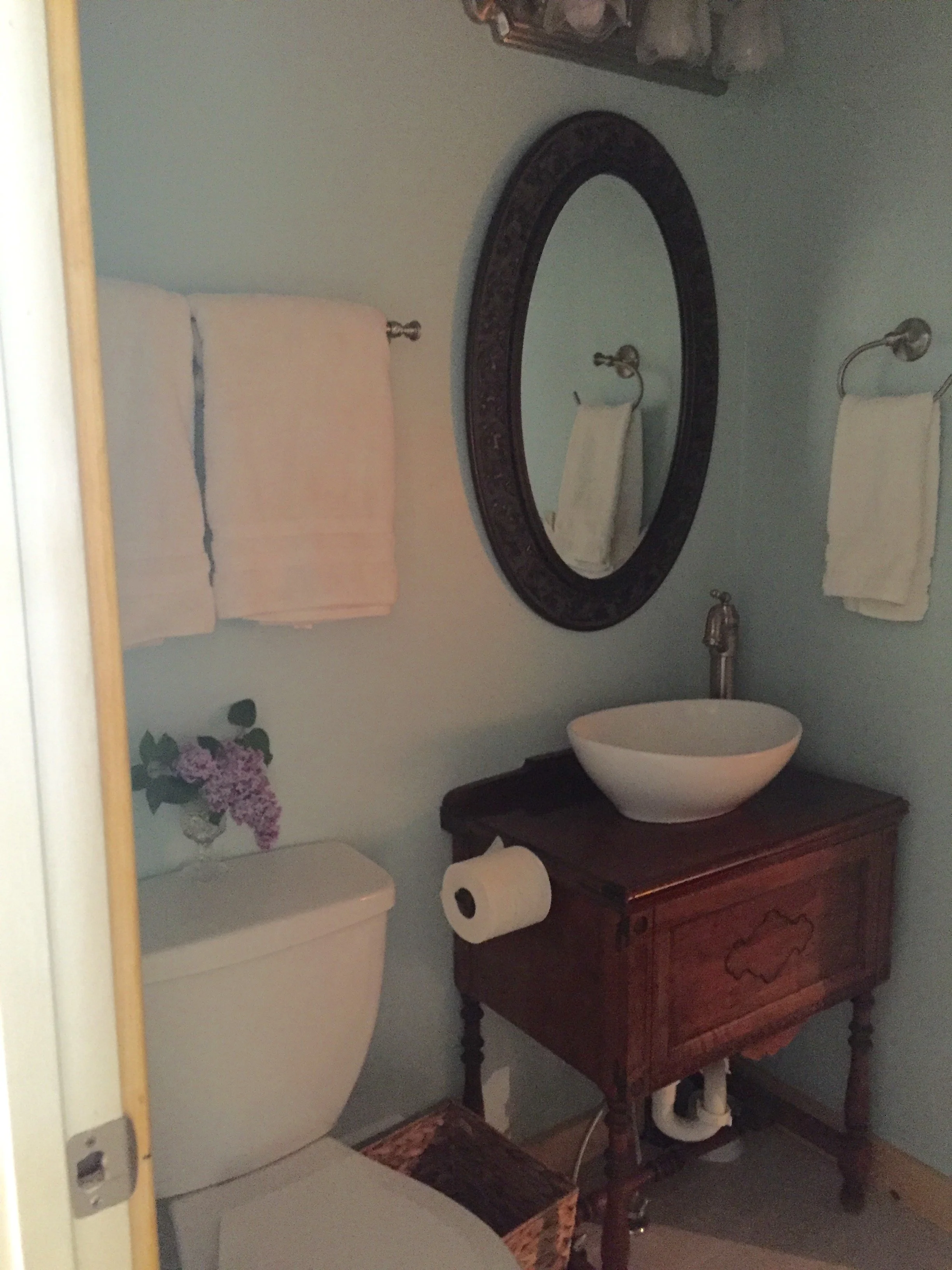 Bathroom with a toilet, a wooden vanity with a bowl sink, a large mirror, and two towels hanging on the wall.