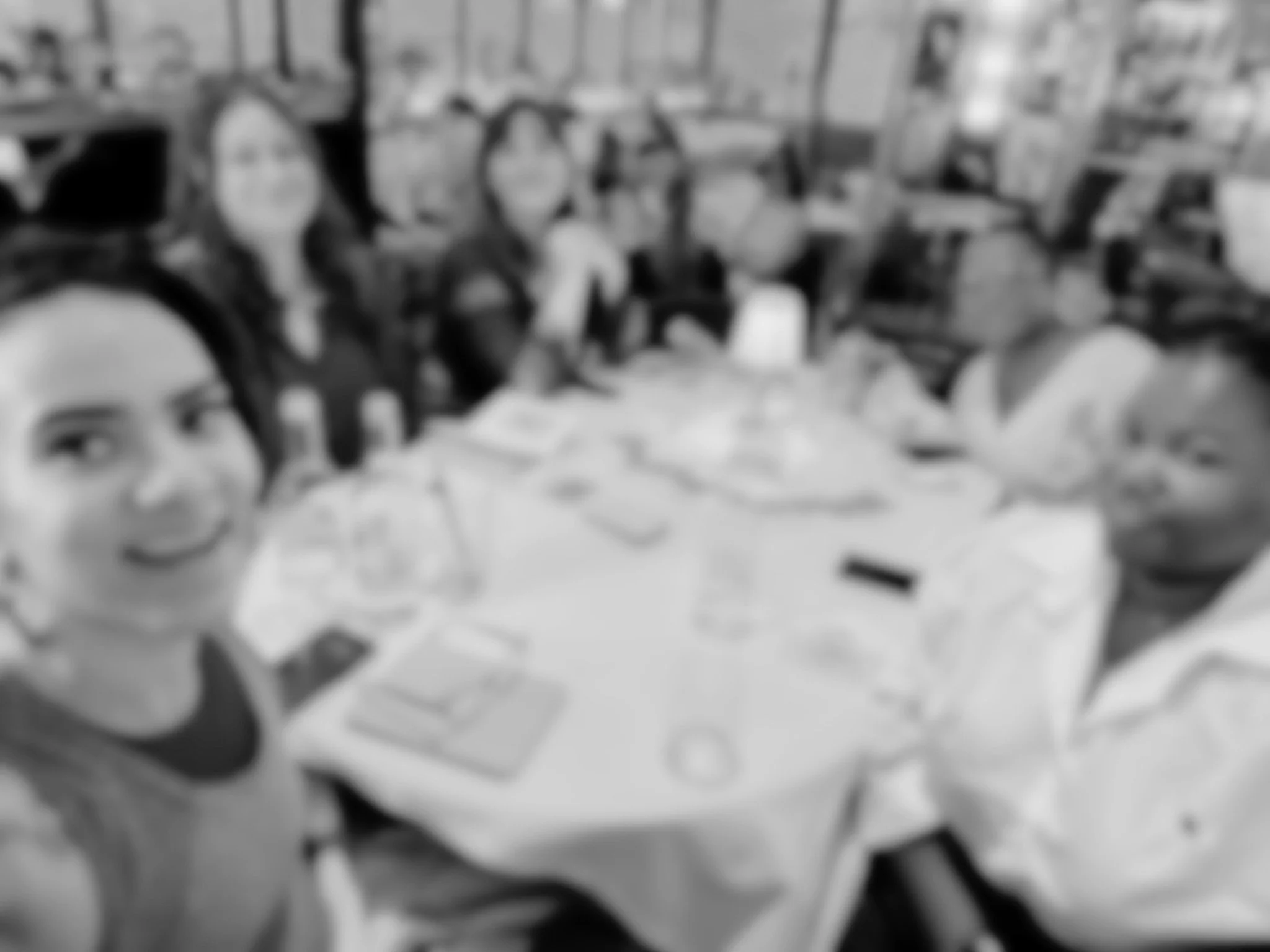 A group of women sitting around a long table in a restaurant or banquet hall, smiling and posing for the photo.