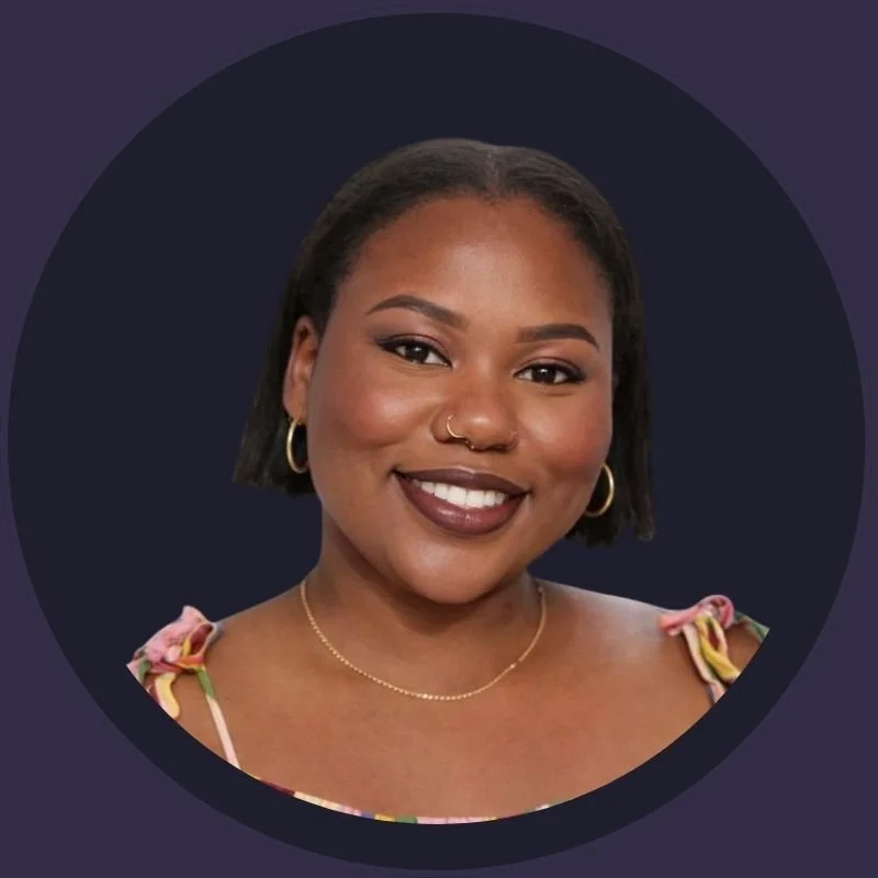 A smiling woman with short black hair, gold hoop earrings, a gold necklace, and a nose ring, wearing a colorful top with flowery shoulder straps, against a dark circular background.