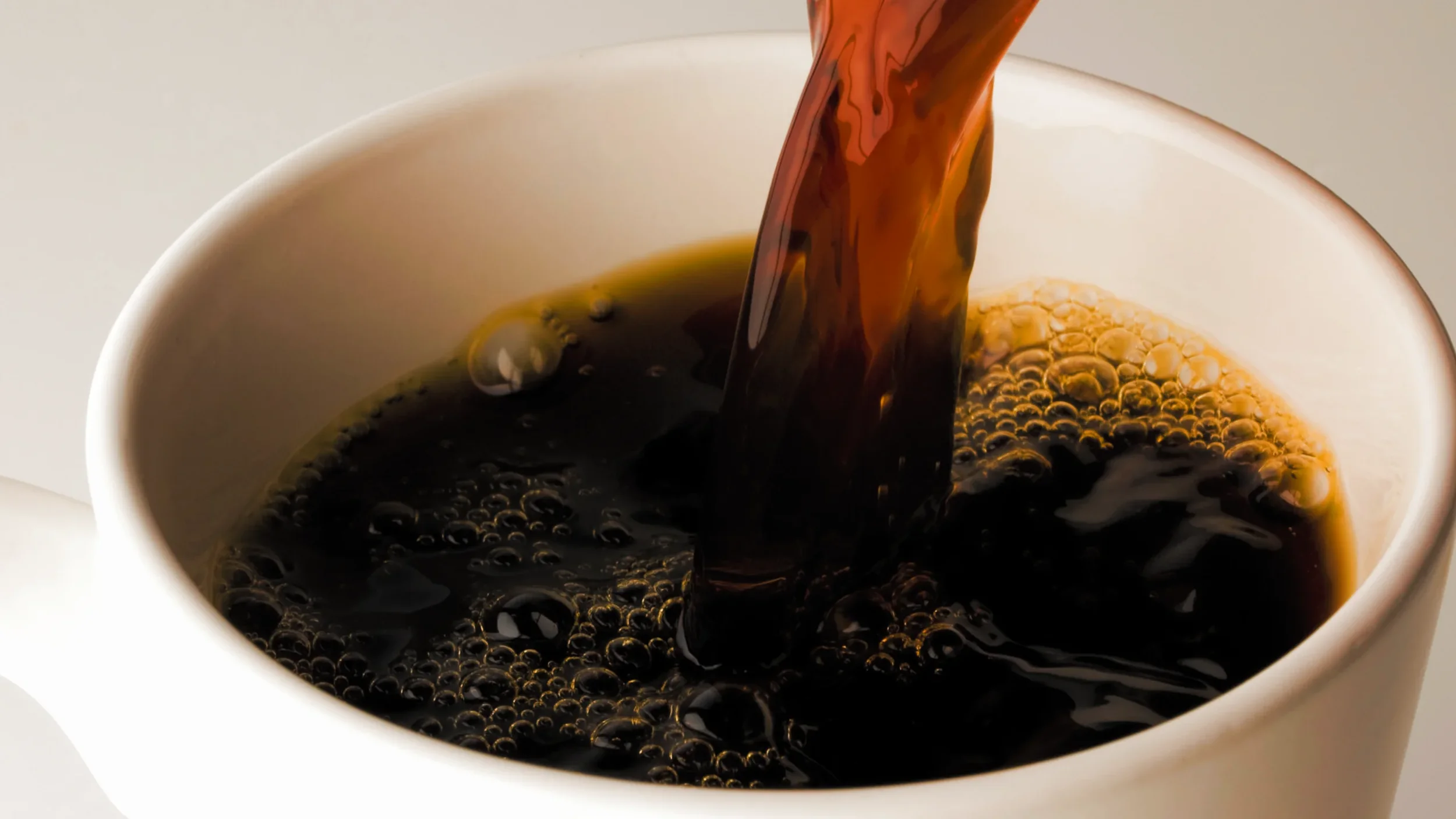Black coffee being poured into a white ceramic cup.