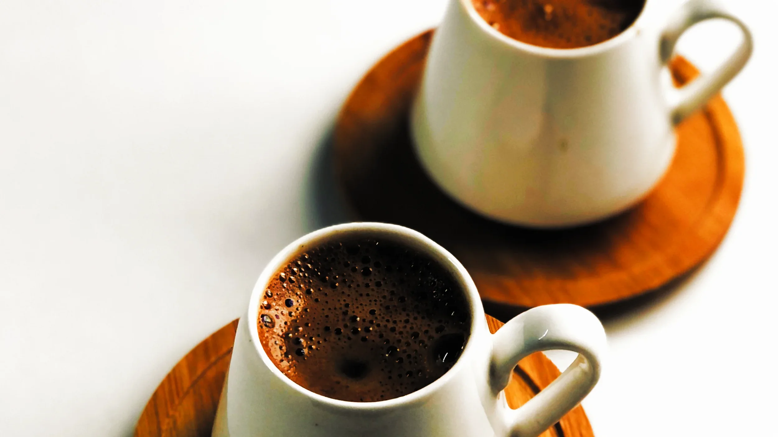 Two white coffee cups filled with black coffee, placed on round wooden trays.