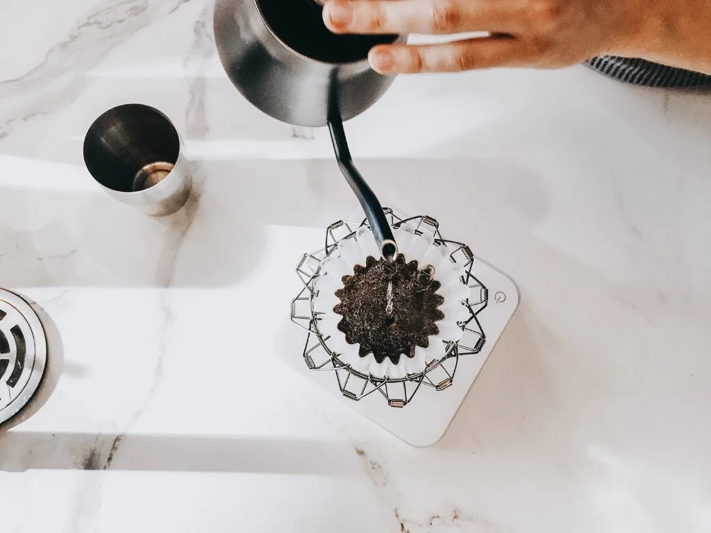 An overhead view of a person pouring water from a kettle into a pourover coffee maker.