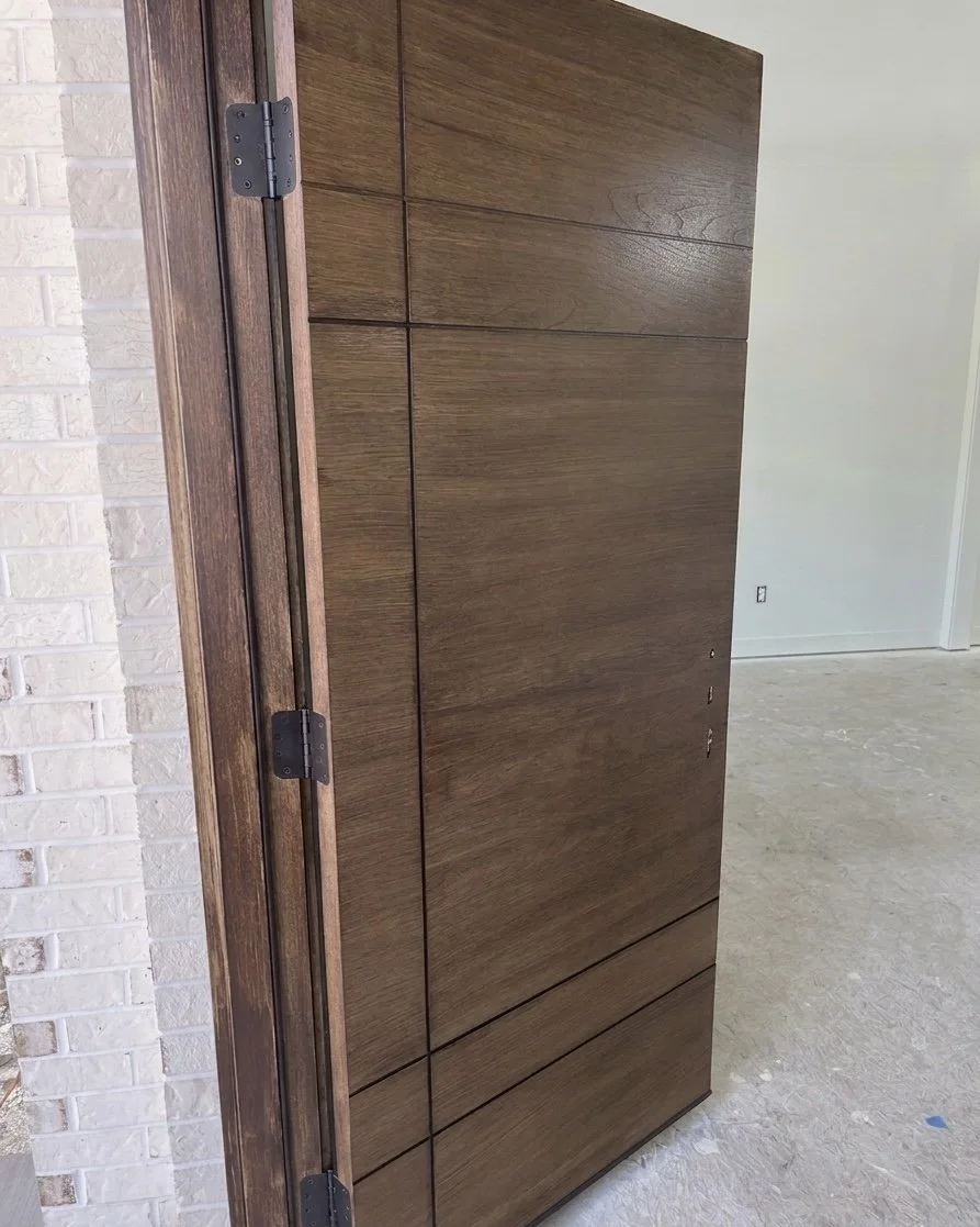 A partially installed wooden door with hinges, leaning against a brick wall in a room under construction.