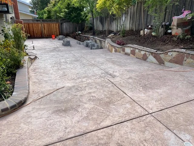 Finished stamped concrete backyard patio with new flower beds and garden decorations.