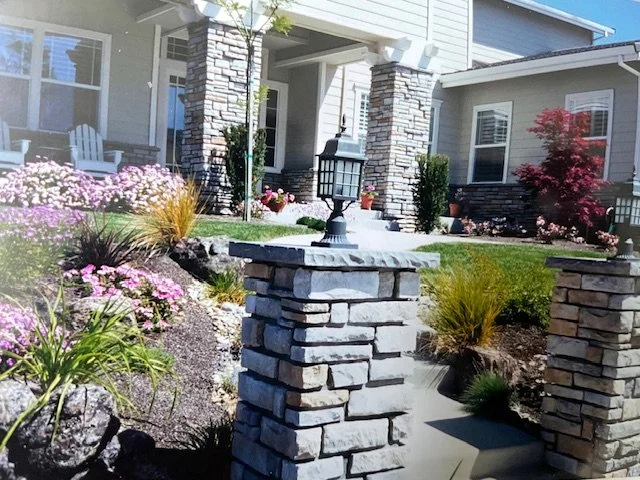 Front yard of a house with stone pillars, a lantern, landscaped garden, and outdoor seating