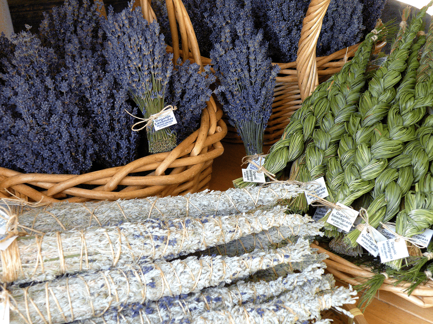 Fresh organic lavender and sweetgrass bundles displayed in wicker baskets at a market.