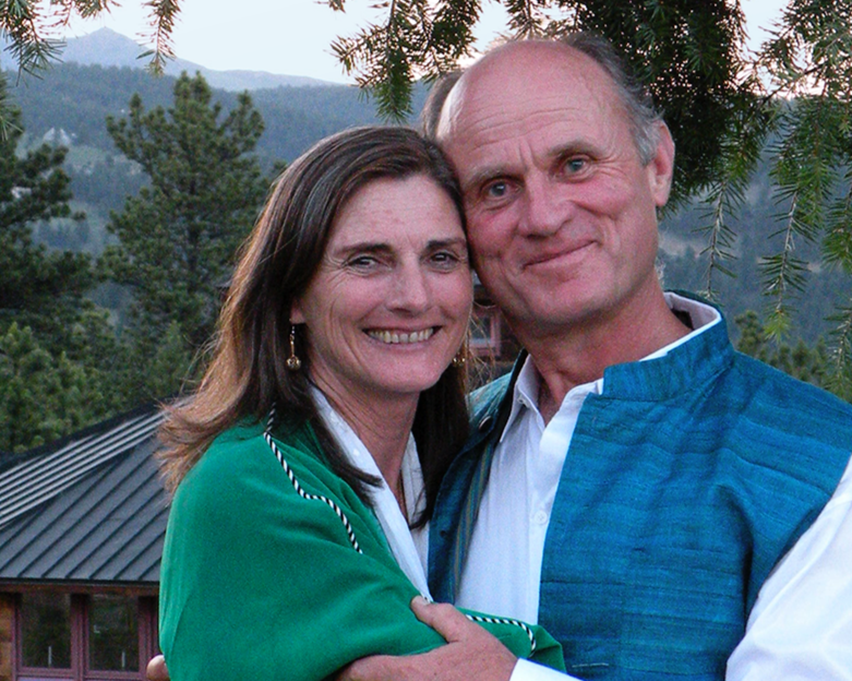 A smiling couple embracing outdoors with a background of trees and mountains during sunset.
