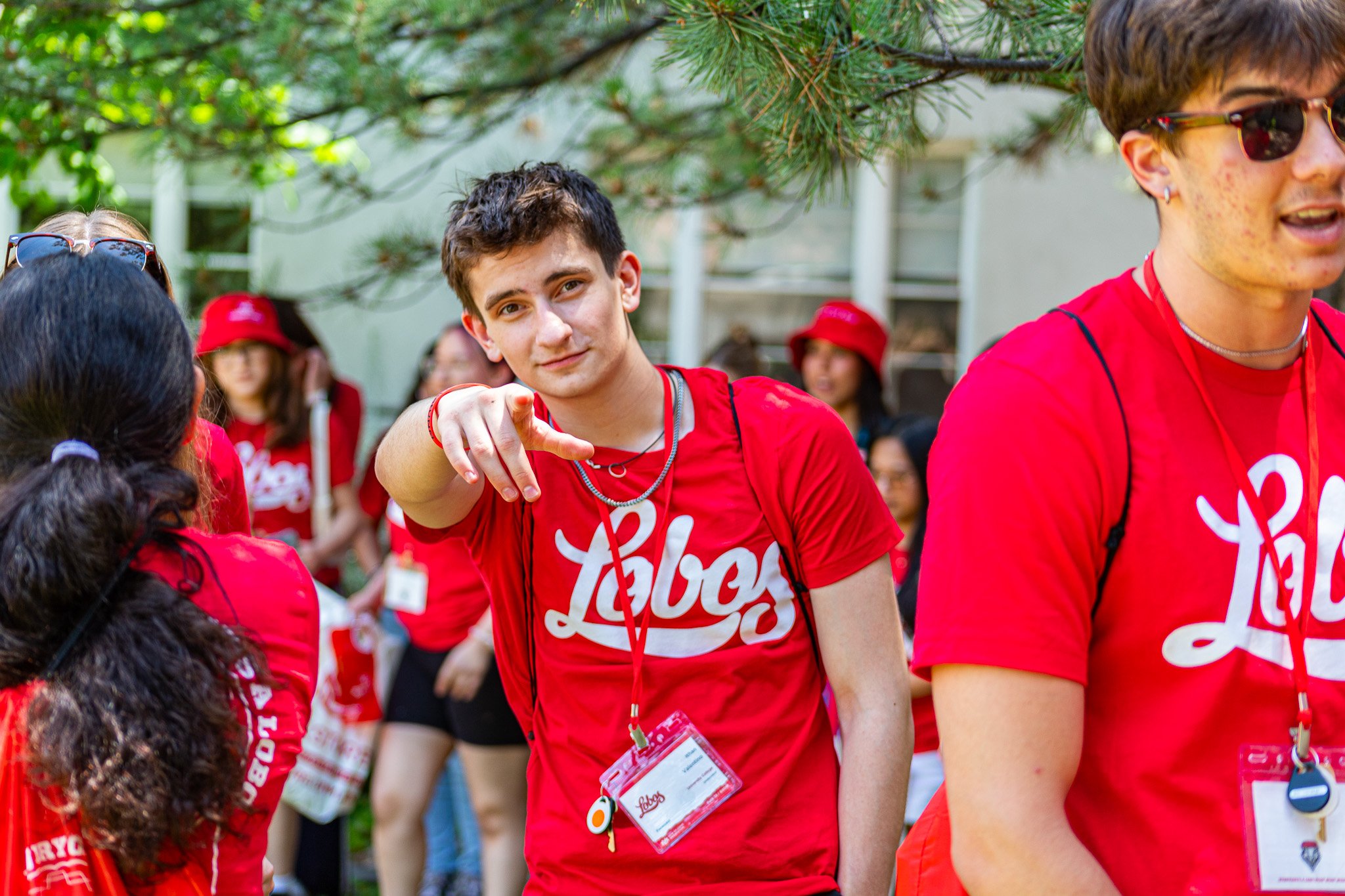 Group of young people wearing red t-shirts and name tags at an outdoor event, with green trees in the background.