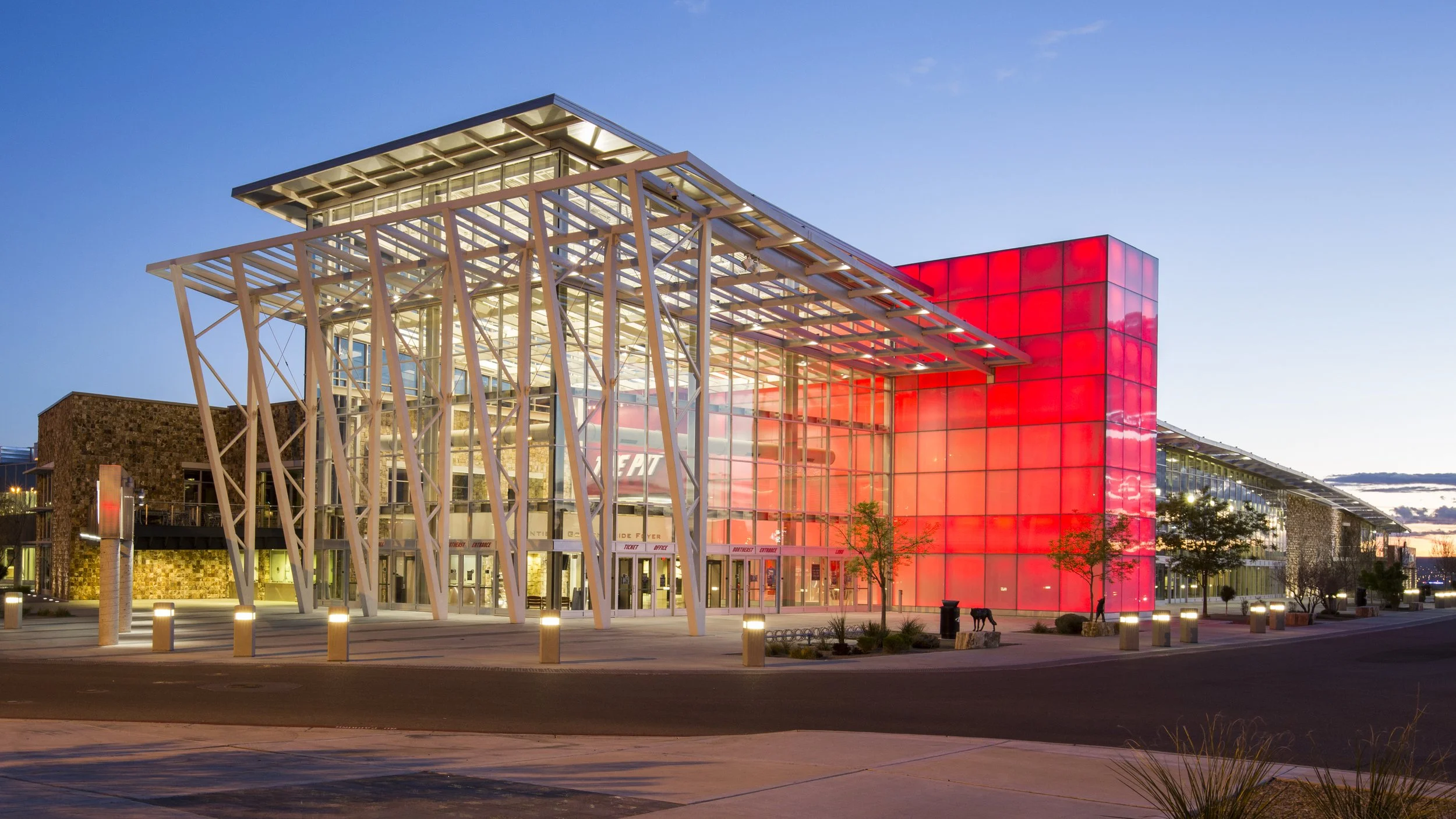 Modern sports arena with glass and metal architecture, illuminated at dusk, featuring a large red illuminated facade.