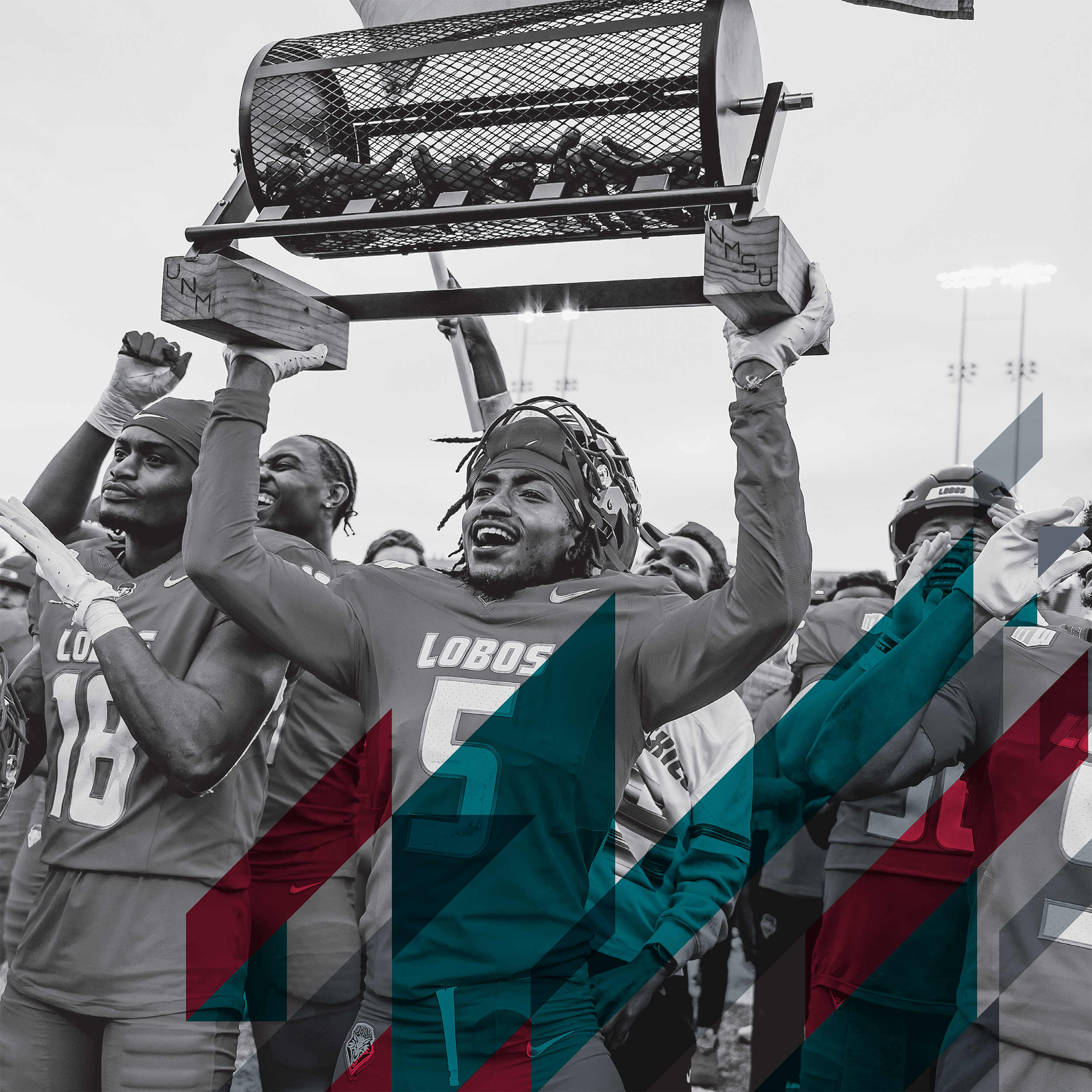 Group of football players, wearing helmets and team jerseys, celebrating as they hold up a trophy after a game.
