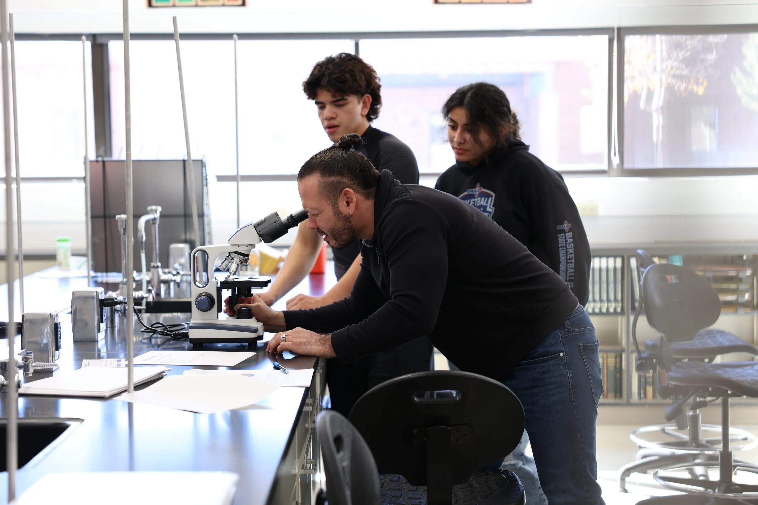 A group of three students working with a microscope in a science laboratory