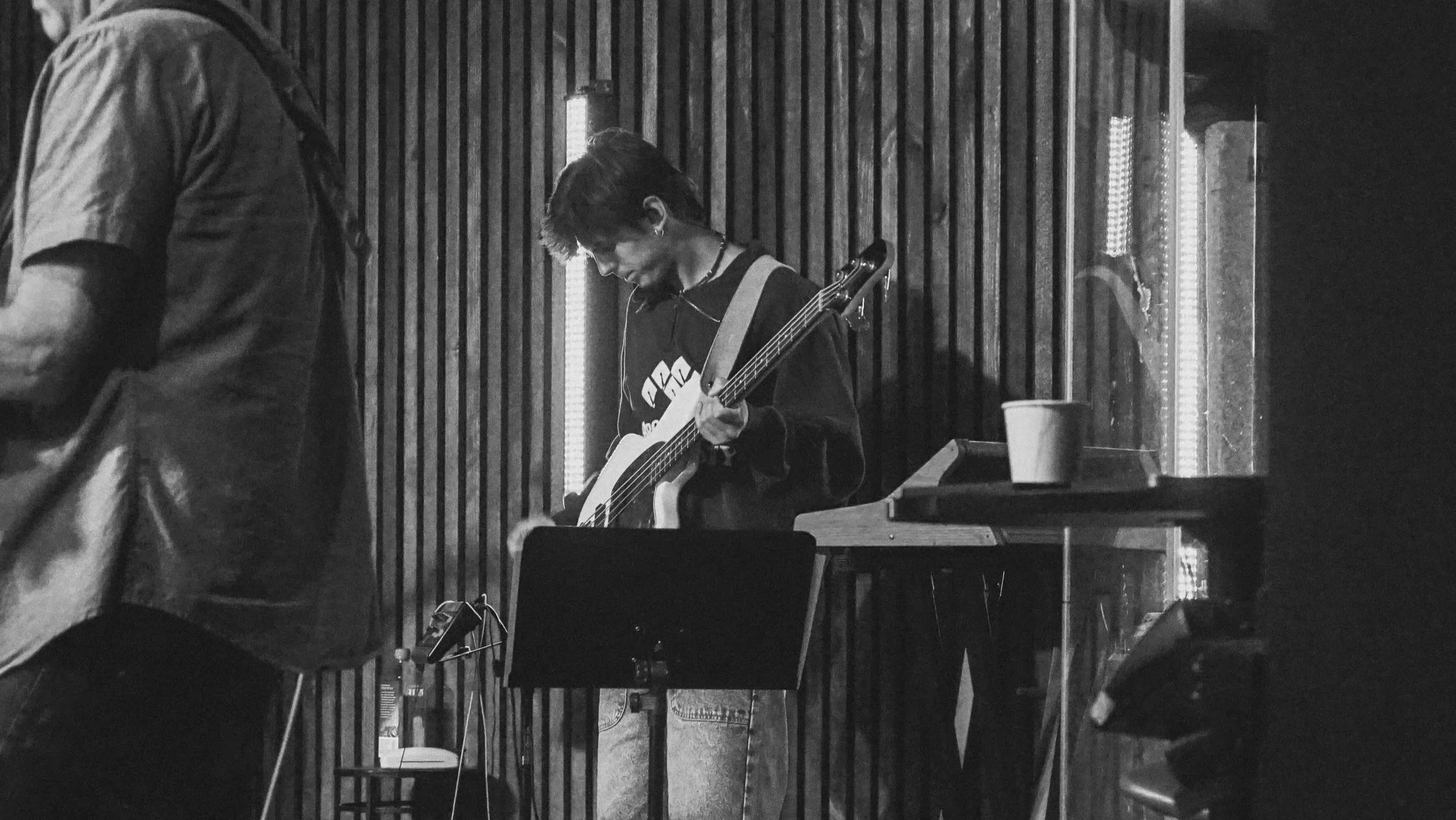 Person playing an electric bass guitar in a recording studio with wooden wall panels and LED light strips.