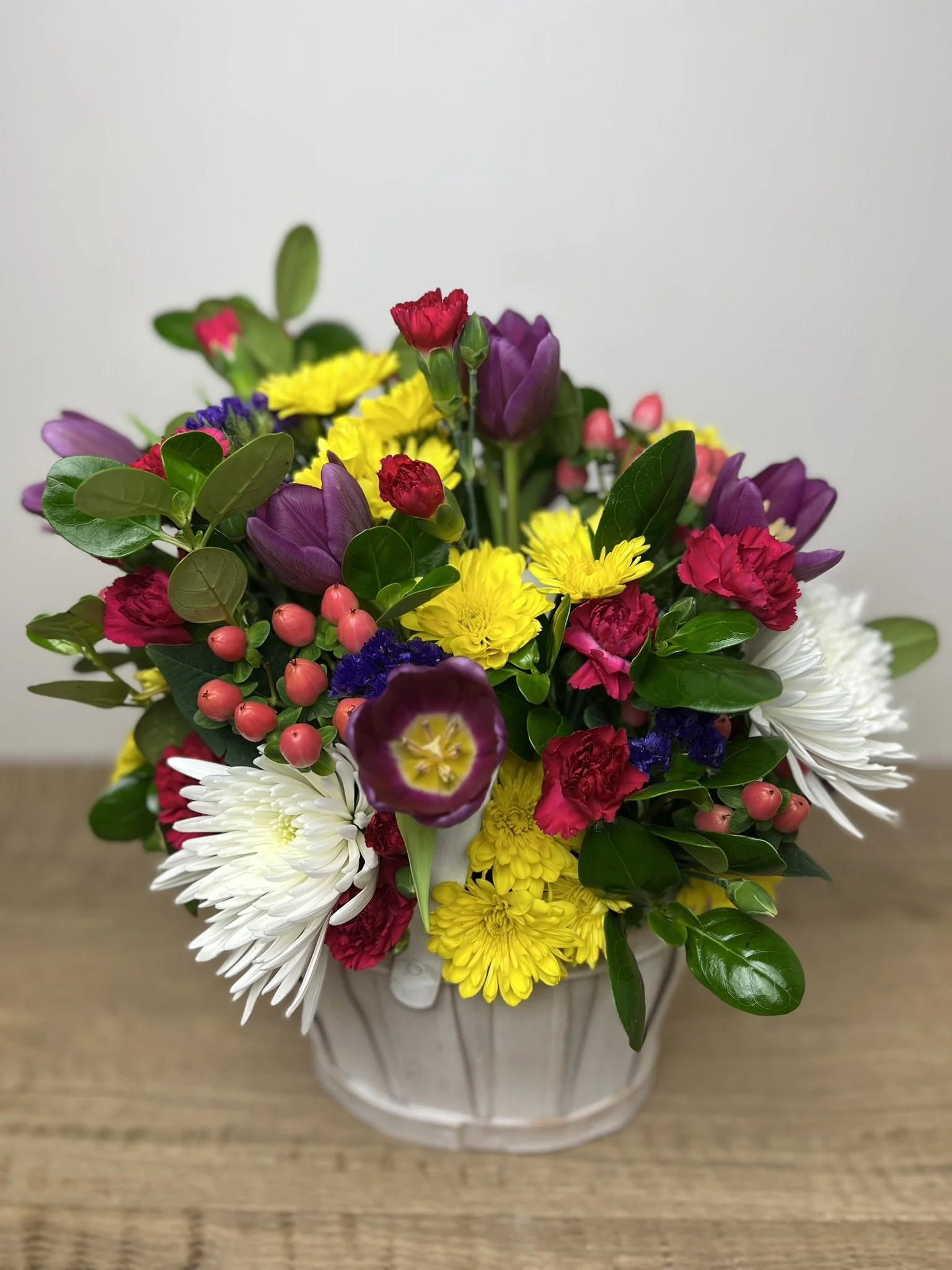 A colorful bouquet of flowers in a white ceramic vase on a wooden surface.
