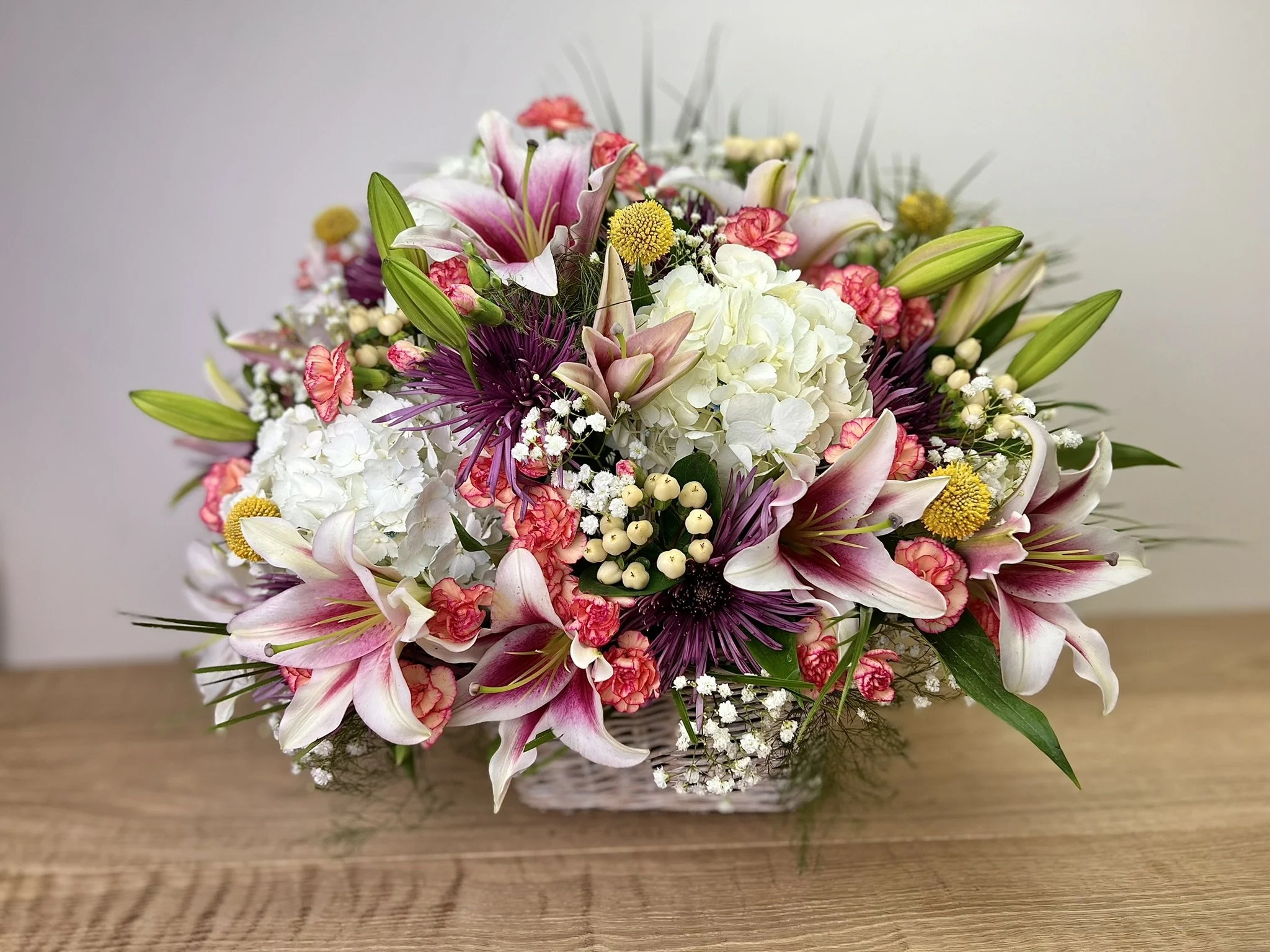 A bouquet of pink, white, and purple flowers in a glass vase on a wooden surface.