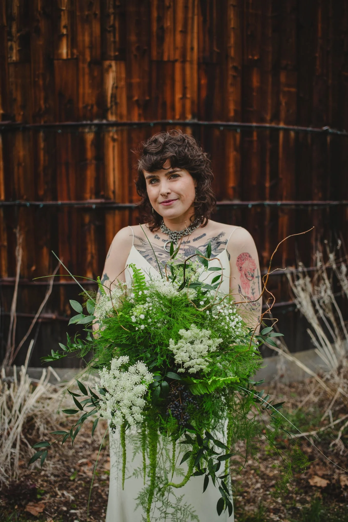 A woman holding a large bouquet of white and green flowers, standing outdoors in front of a wooden fence.
