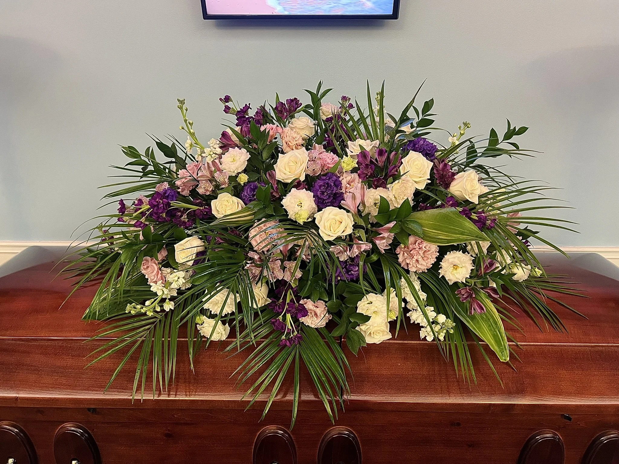 A large floral arrangement with pink, white, and purple flowers on a polished wooden table against a plain light-colored wall.