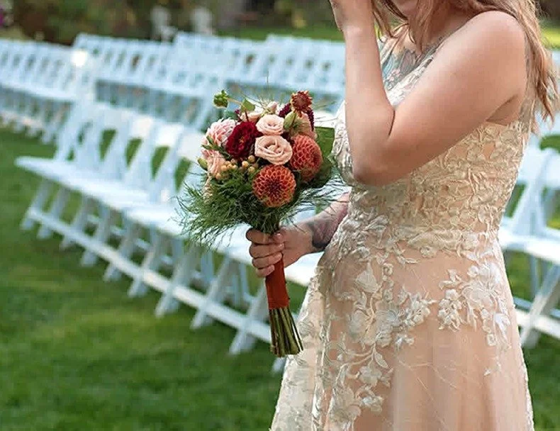 Bride holding a bouquet of flowers on a garden wedding setting with white chairs arranged in rows.