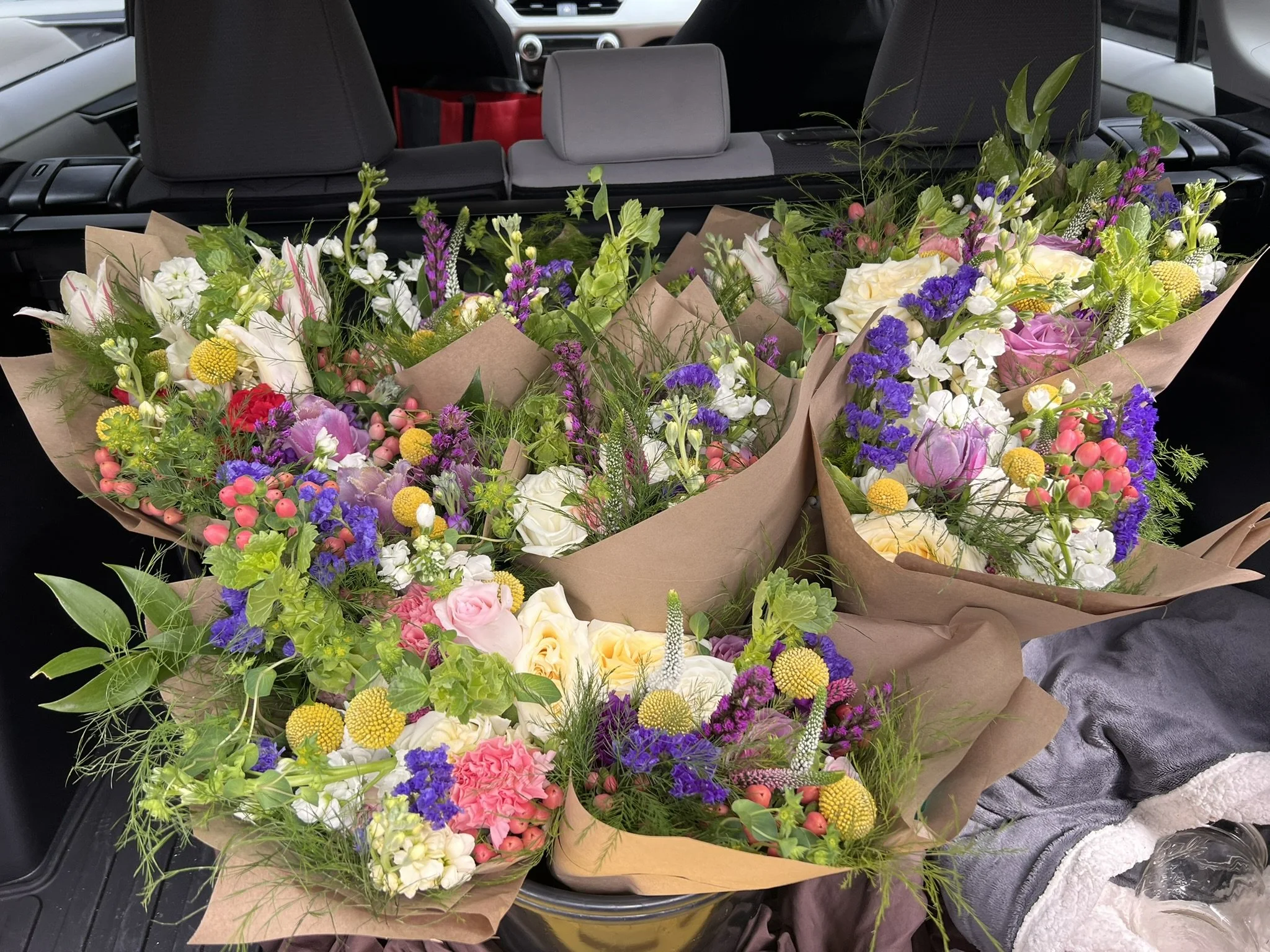 Multiple large bouquets of colorful flowers in brown paper wrapping inside a car