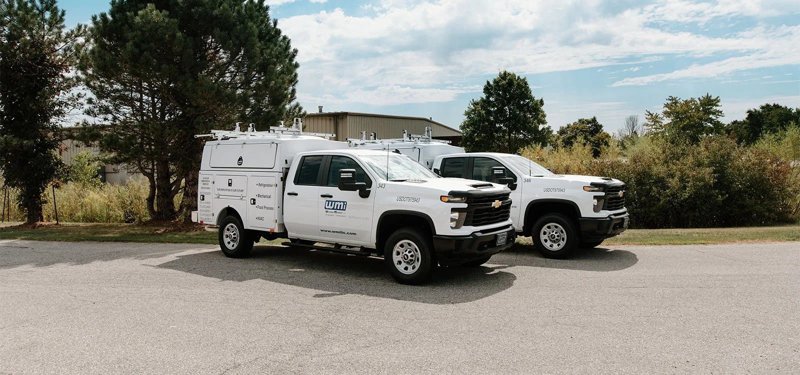 Two white WMI utility trucks parked on the side of a paved road.