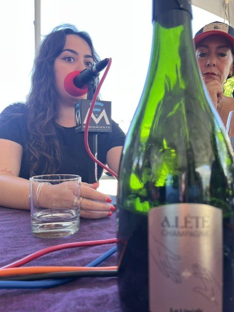 girl speaking into microphone next to bottle of wine