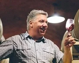 Man smiling and holding a glass of red wine. Bart Hansen of Dane Cellars in the cellar tasting red wine.