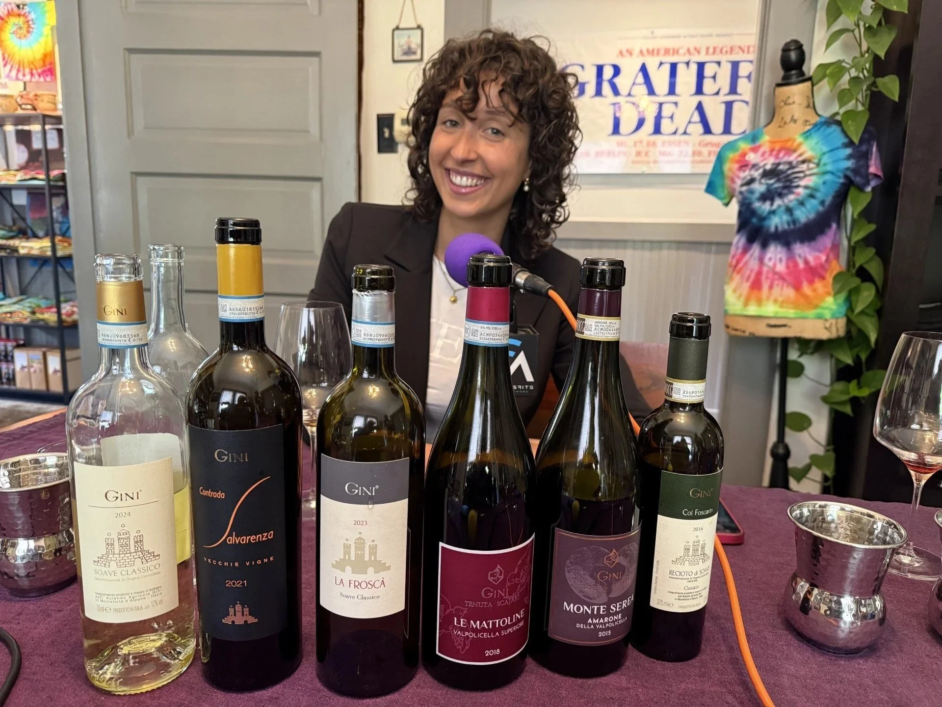 Woman sitting next to microphone and open bottles of wine