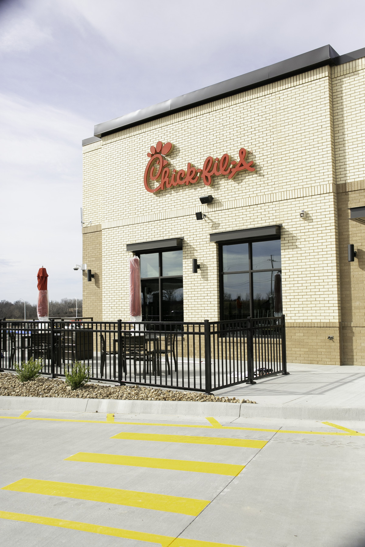 Chick-fil-A restaurant with outdoor seating area, closed umbrellas, and a parking lot with yellow striped crosswalks.