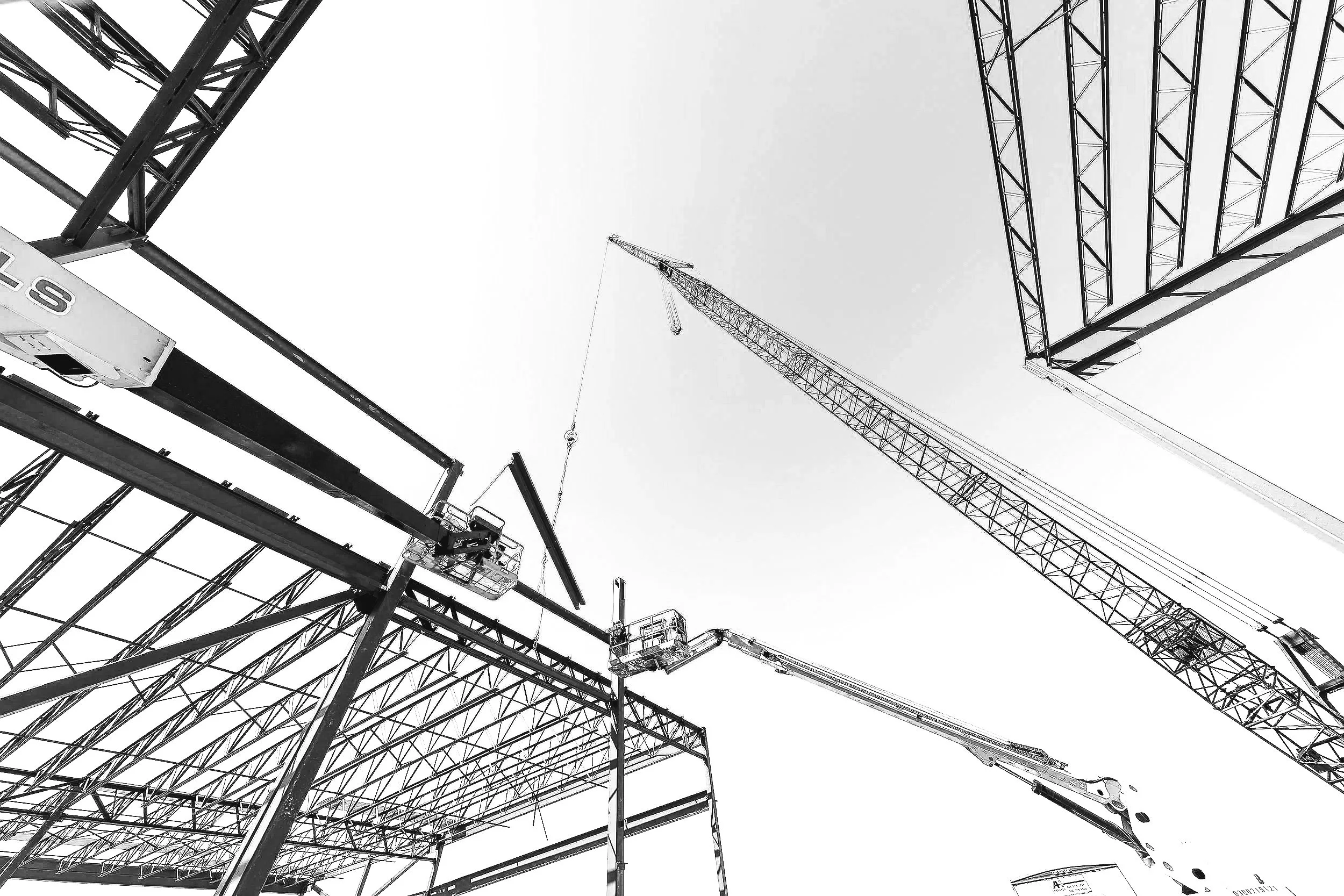Construction site with cranes and steel framework seen from ground level in black and white.